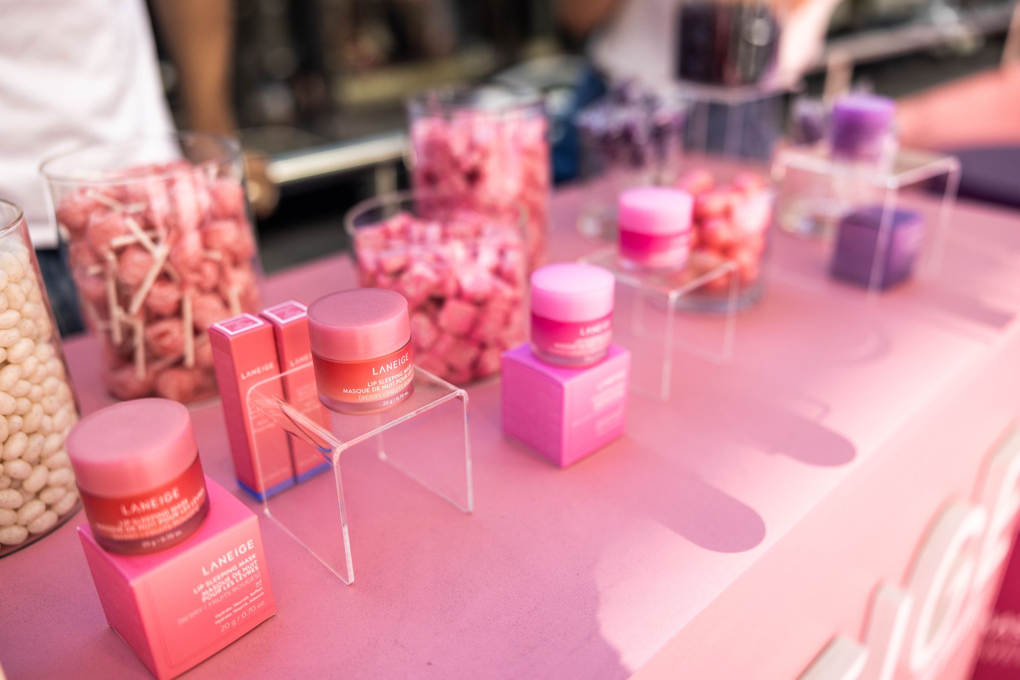 Pink and purple Laneige skincare on stands atop a pink table, with candy jars in the background.