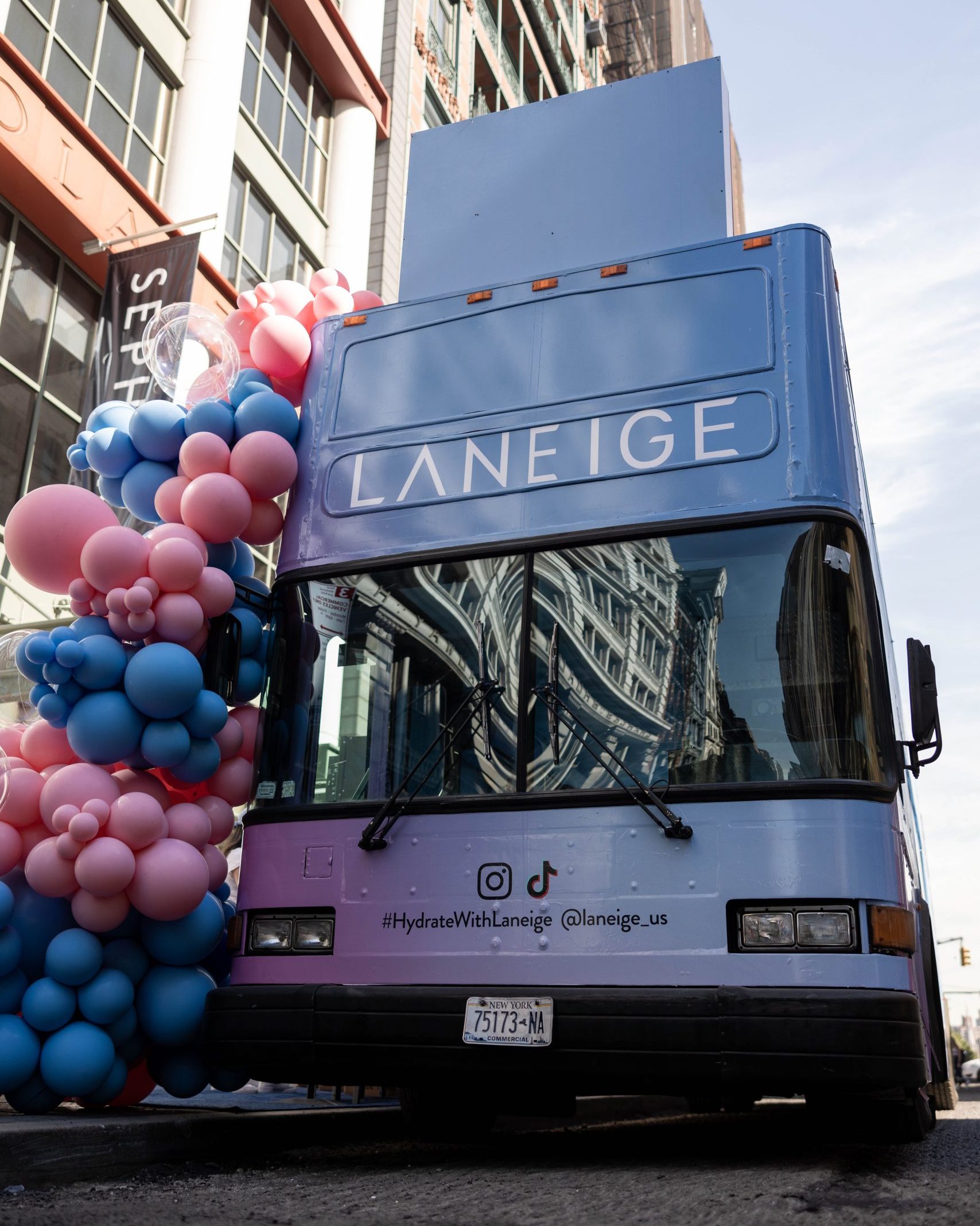 A double-decker bus with pink and blue balloons and Laneige branding is parked on a city street.