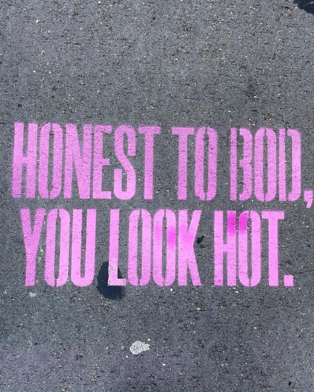 Pink spray-painted text on a concrete sidewalk reads HONEST TO BOD, YOU LOOK HOT in all caps.