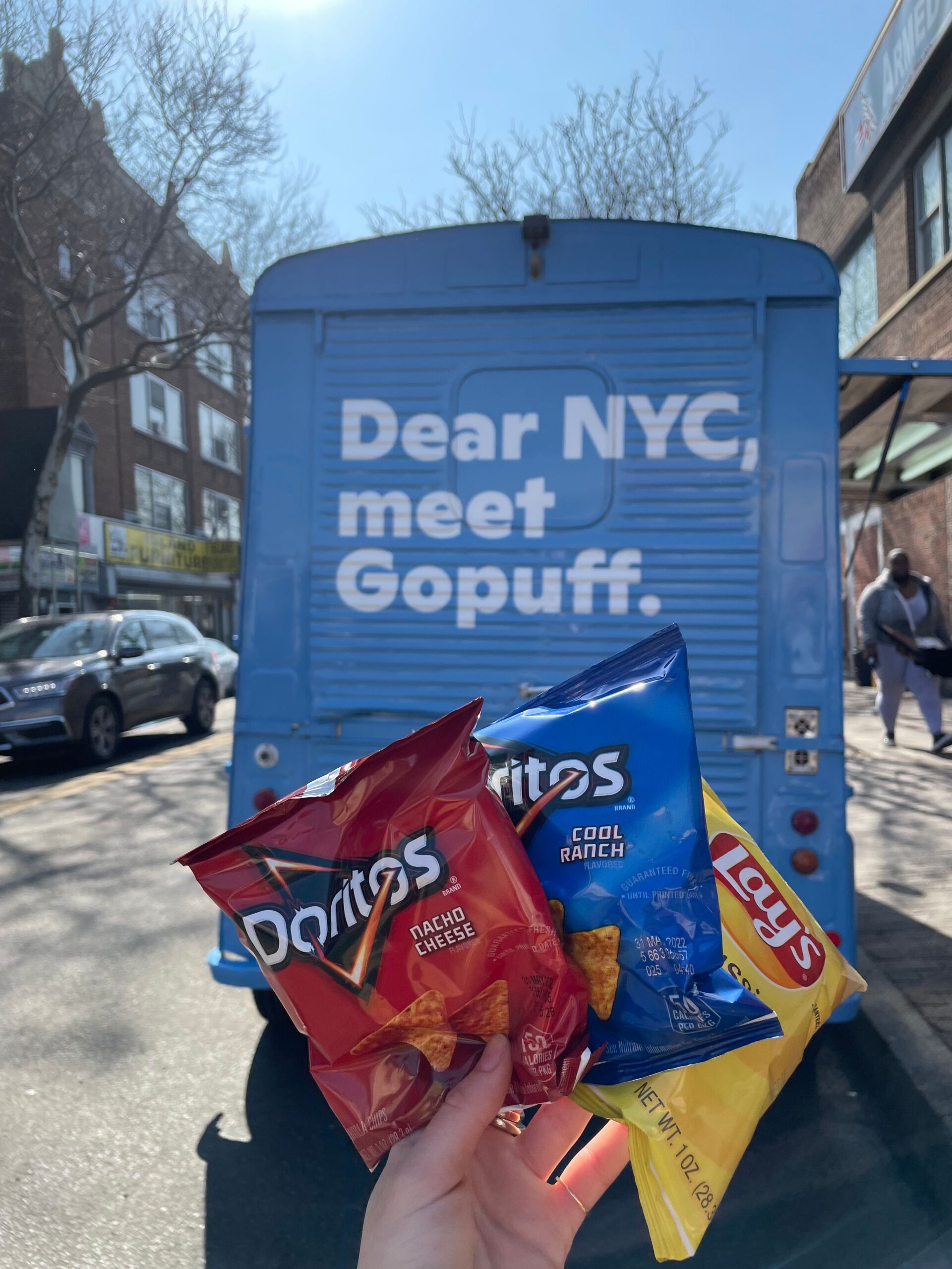 Hand holding Doritos and Lay's chips in front of a blue truck with “Dear NYC, meet Gopuff” text.