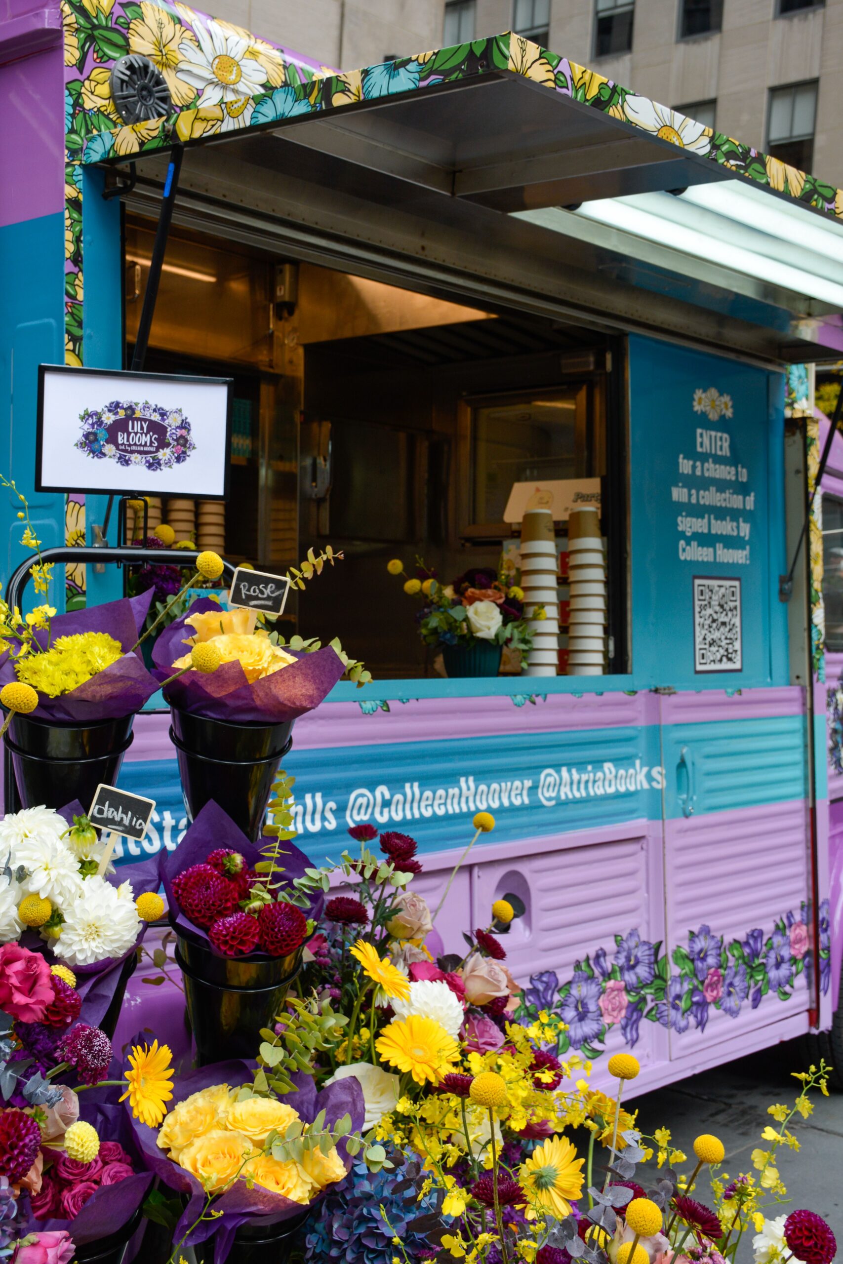 Pastel blue, pink, and purple floral food truck with "it starts with us" signs and flowers in front.