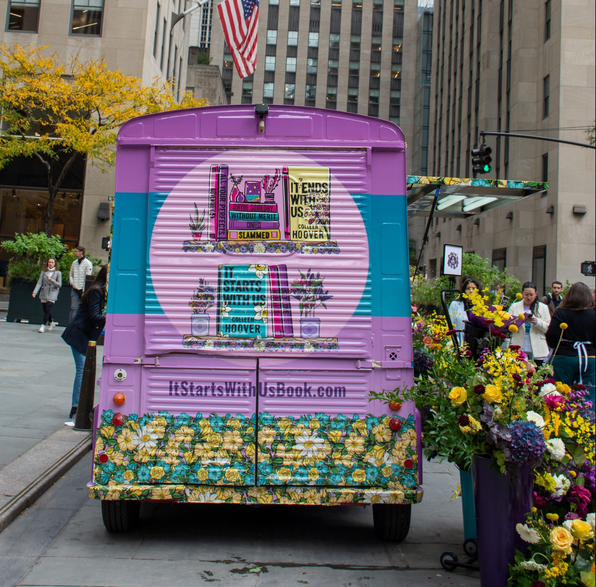 A book-themed truck with flowers promotes ItStartsWithUsBook.com on a city street.