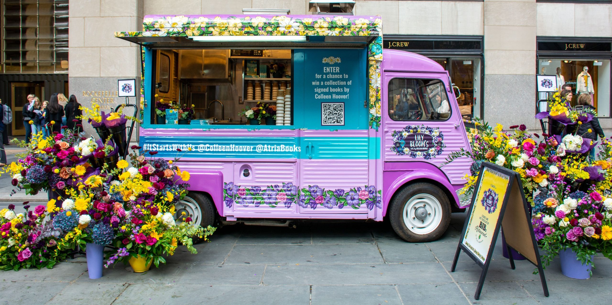 Pastel purple and blue vintage food truck with "It Starts With Us" sign, flowers around it.