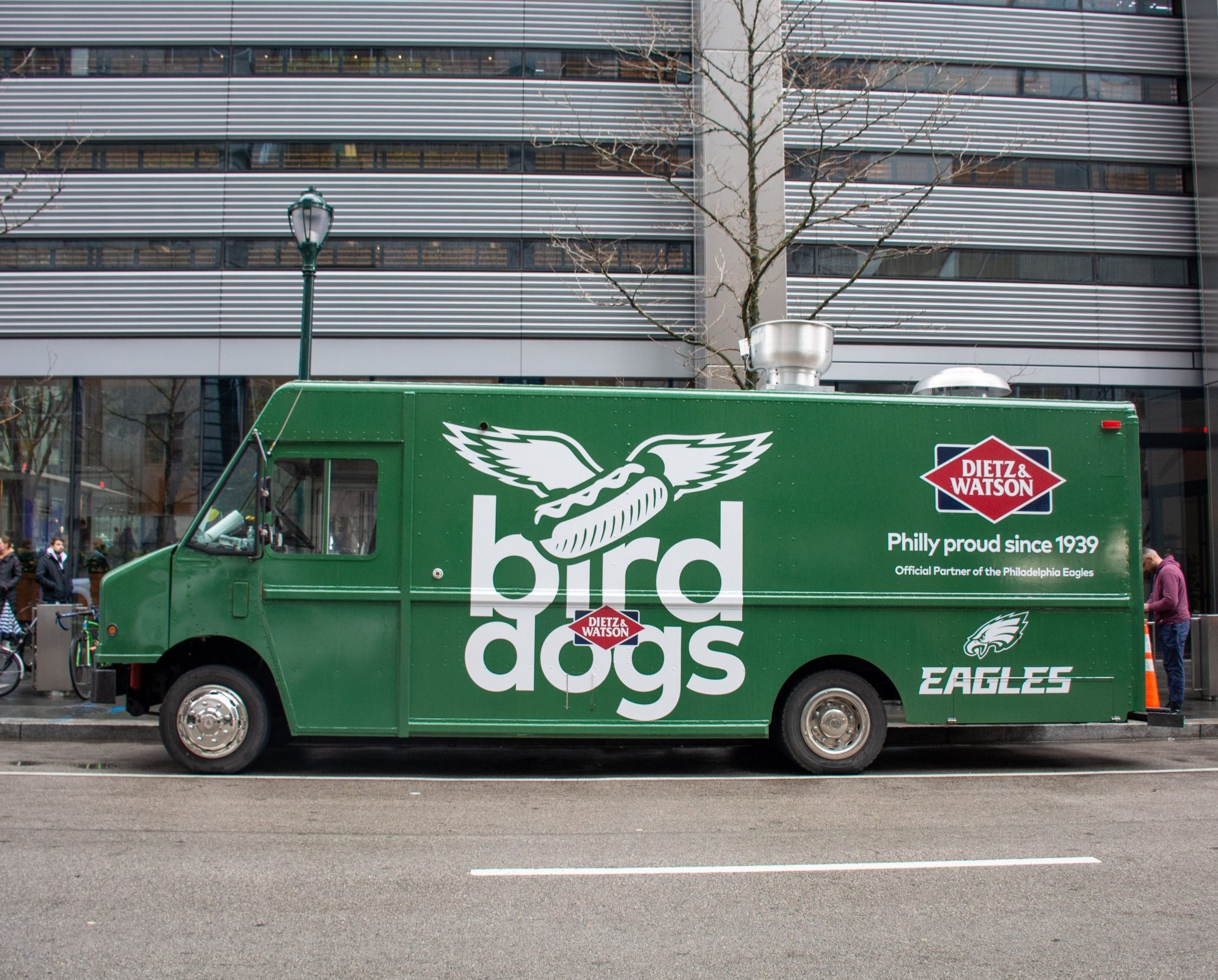 Green Bird Dogs truck with Dietz & Watson and Eagles logos, parked on a city street.