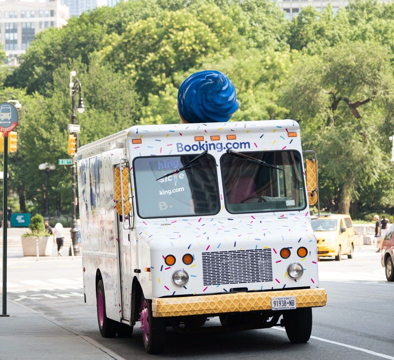 Booking.com ice cream truck with sprinkles and blue swirl drives down a city street.