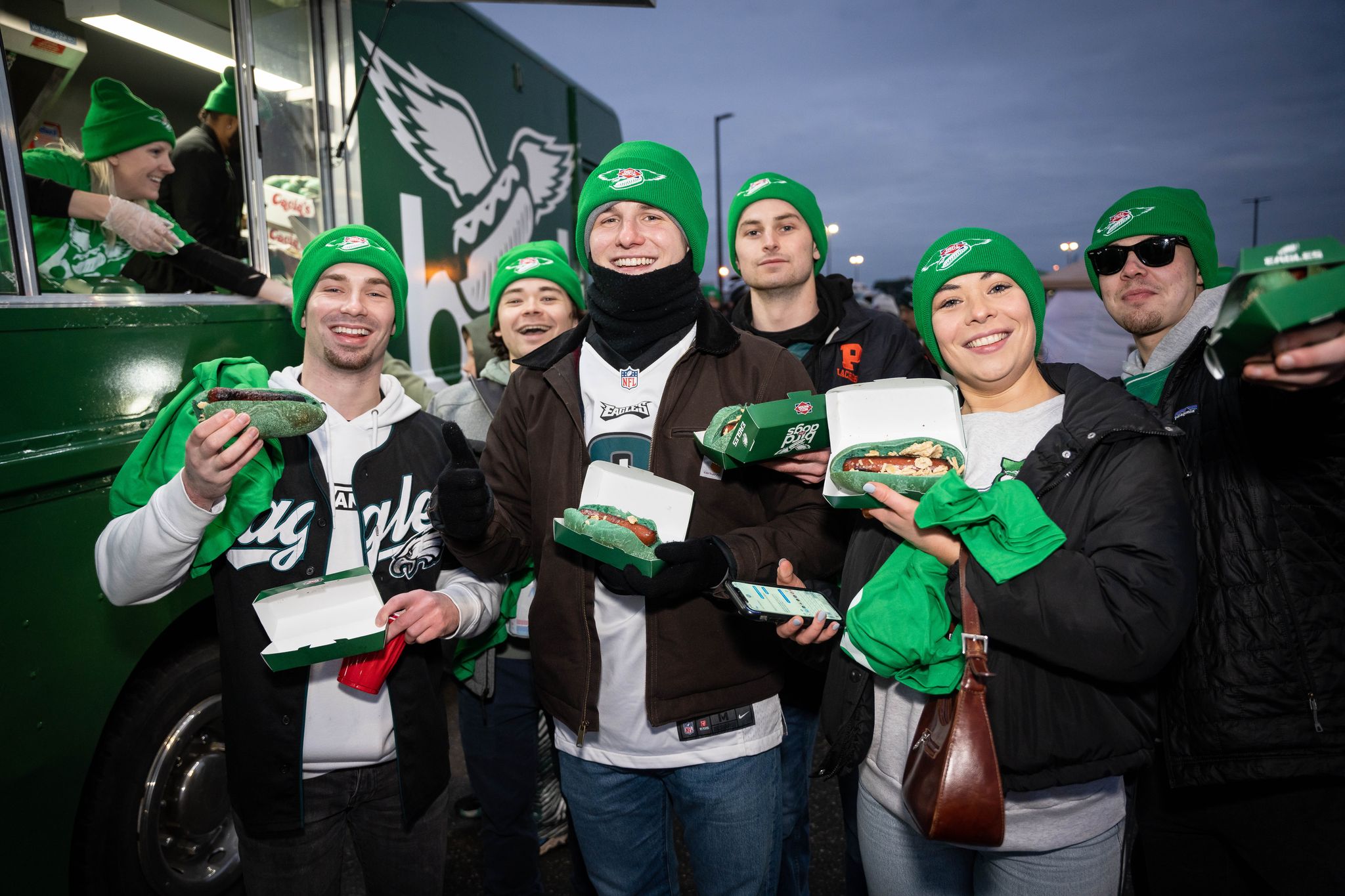 People in green Eagles gear pose with hoagies outside the Bird Dog Truck, celebrating together.