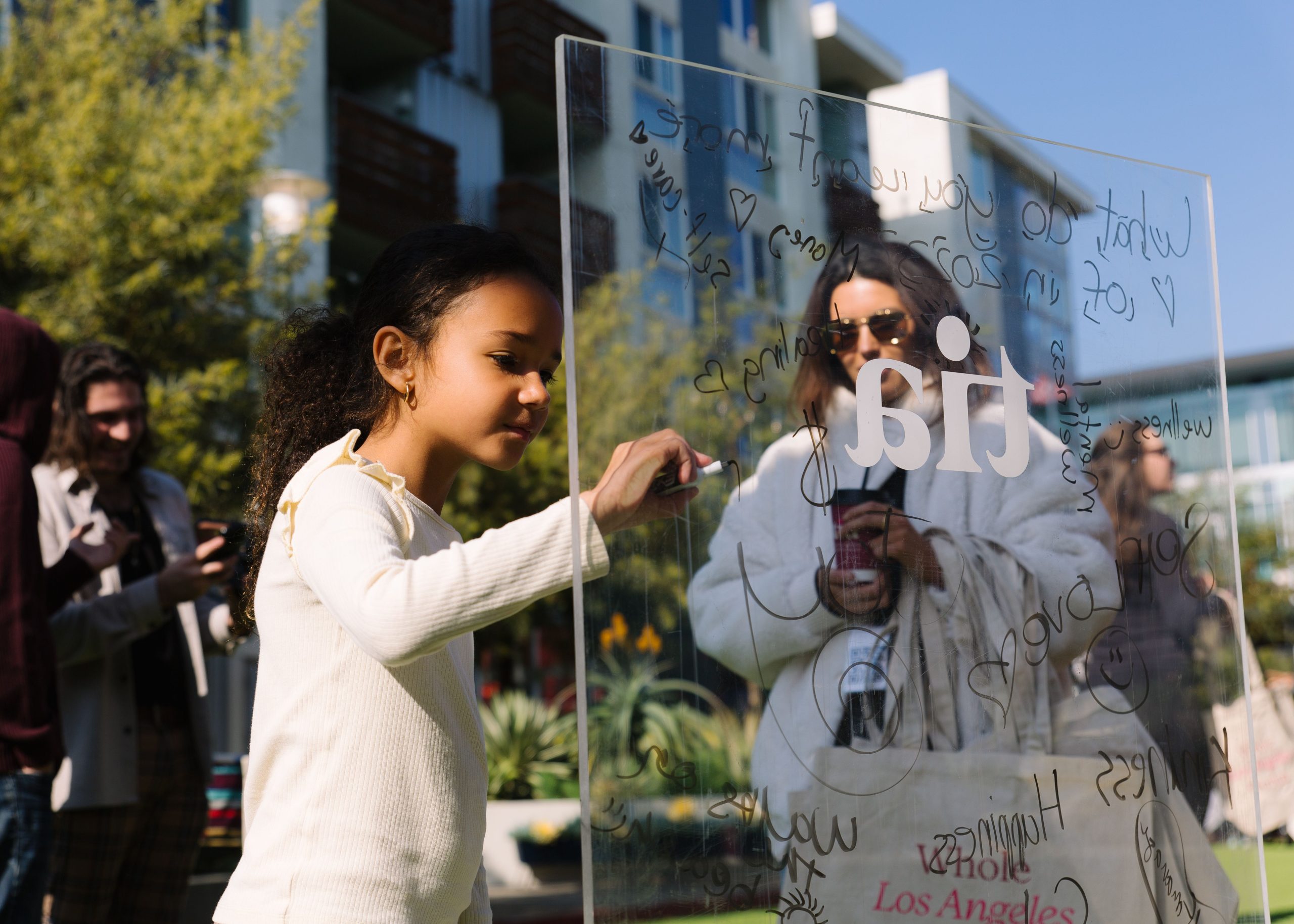 A little girl using marker to write on a glass board at Tia's pop-up