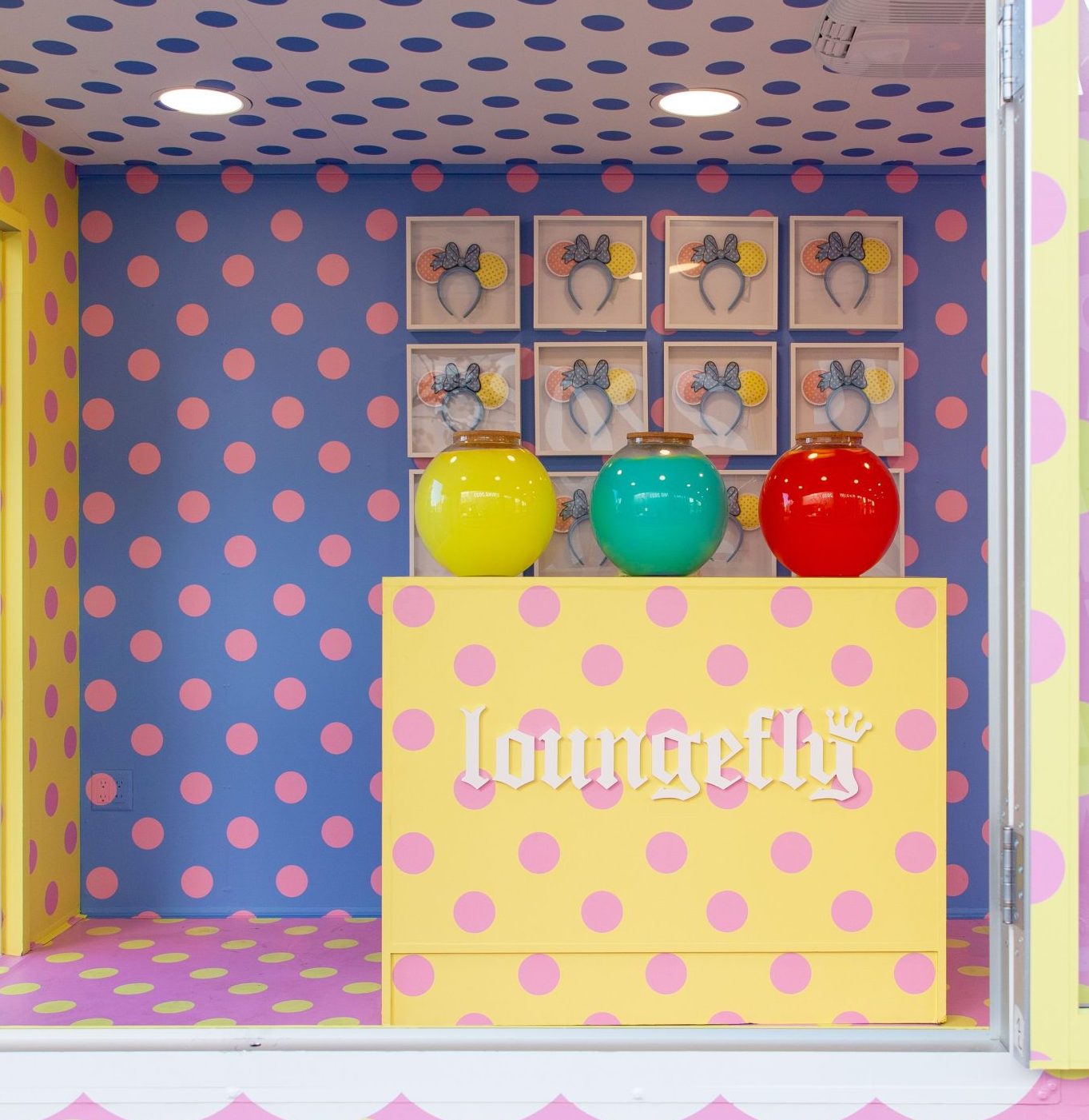 Yellow Loungefly counter with three jars, nine bow frames, pink polka dots on blue and yellow walls.