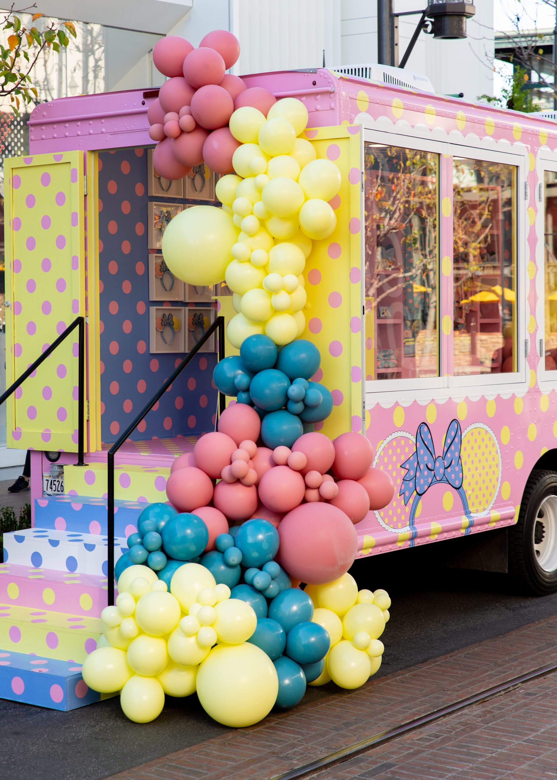 Polka dot pop-up truck with blue bow and yellow, pink, teal balloons cascading to the ground.