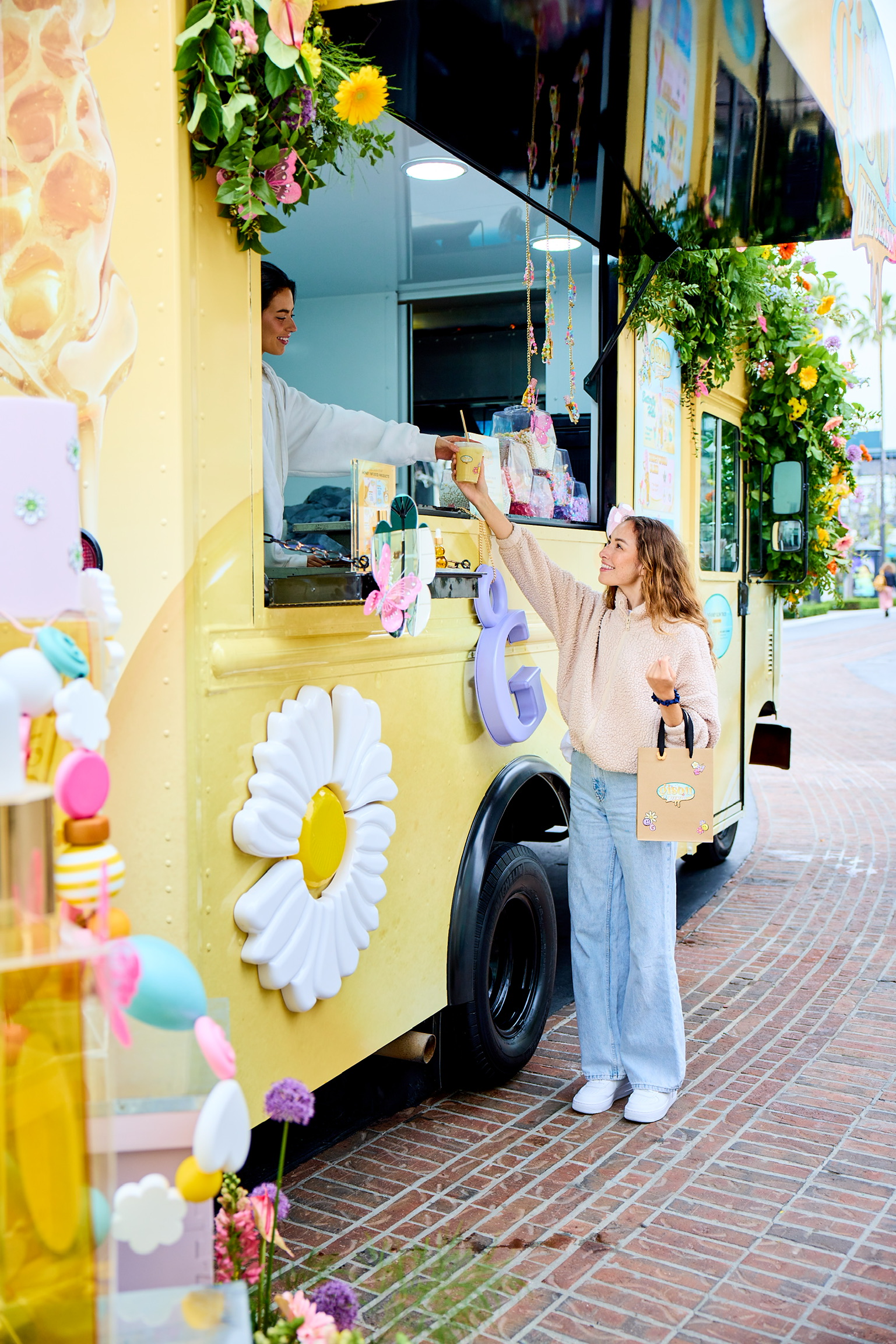 A woman reaches up for a drink from a smiling server in a bright yellow Gisou food truck.