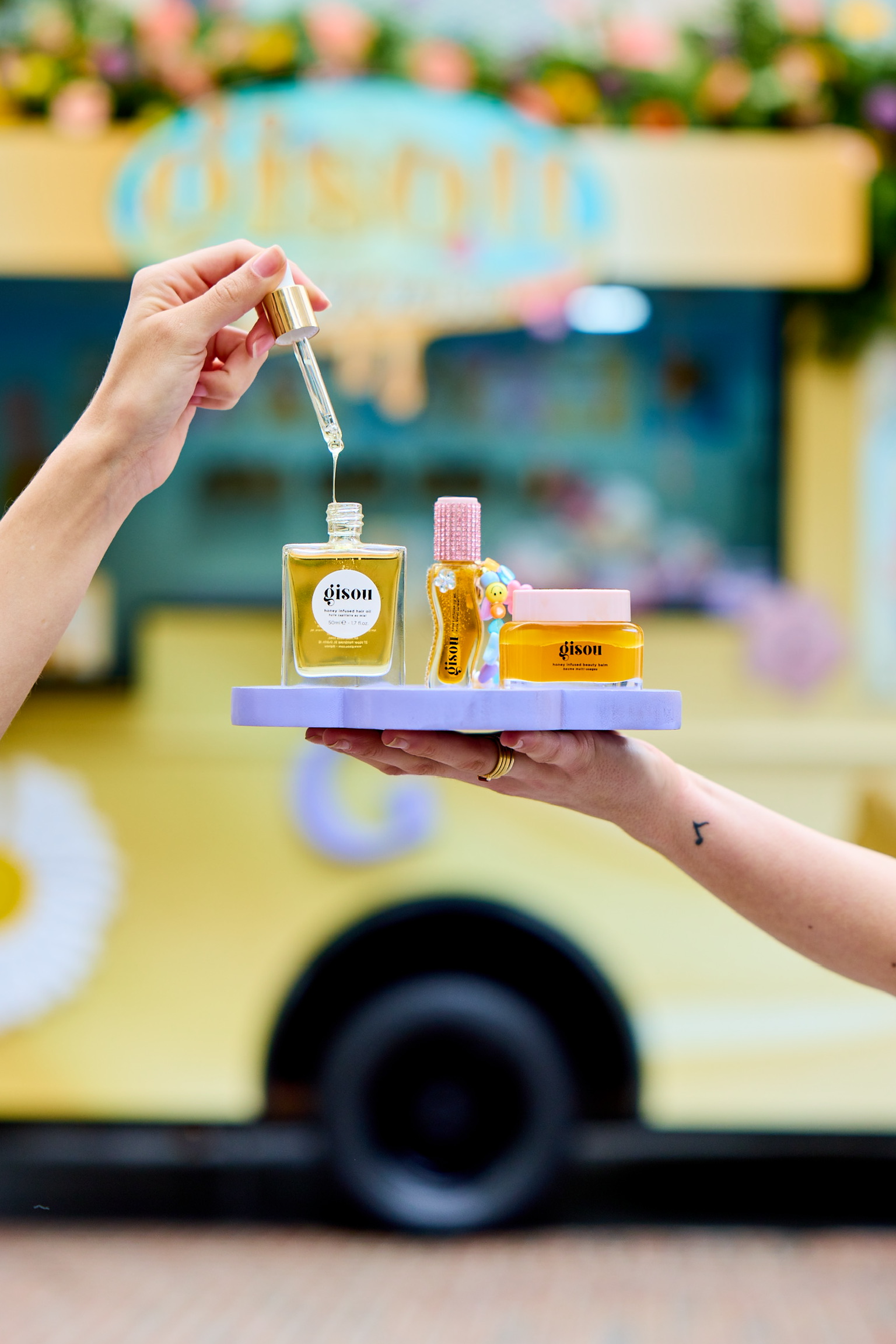 A person holds a dropper over a Gisou hair oil bottle with other Gisou products nearby on a tray.