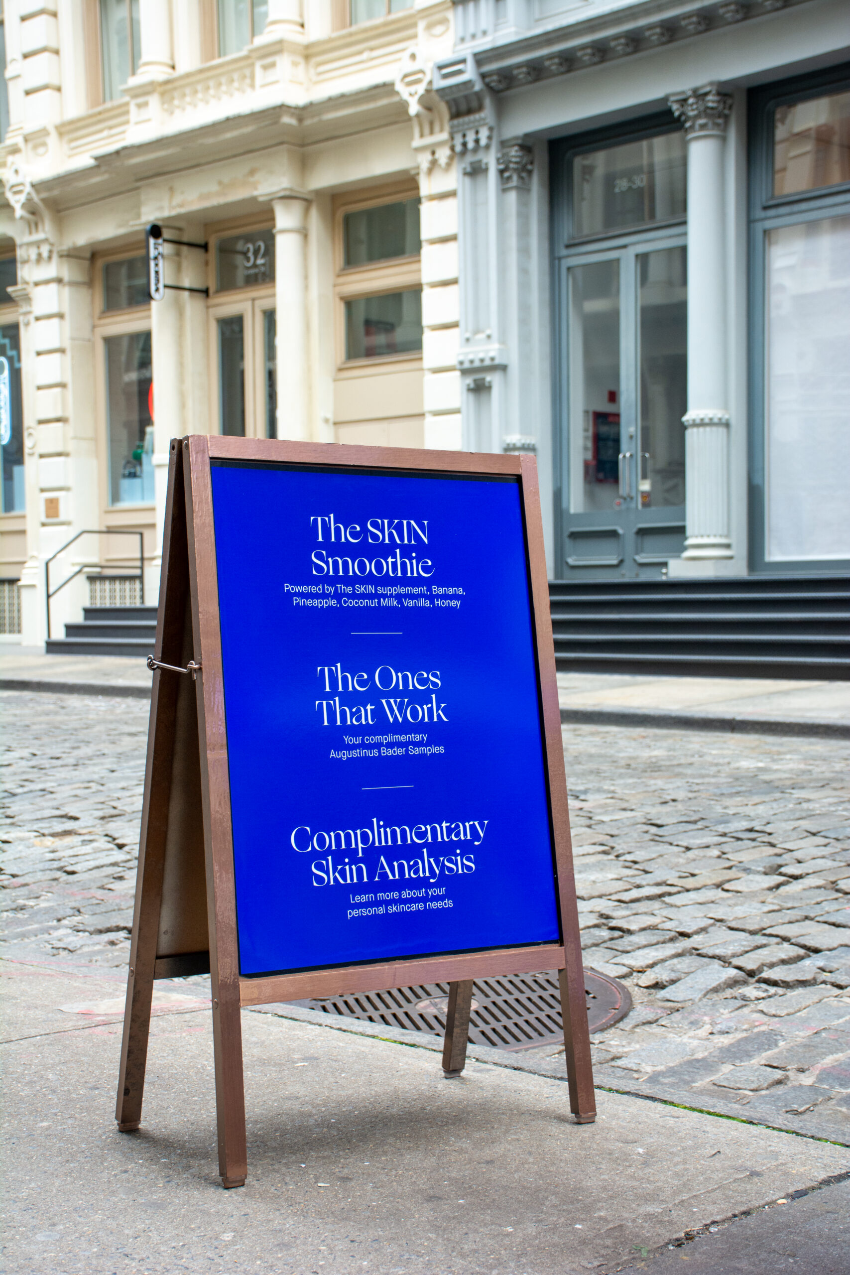Blue sandwich board advertises Augustinus Bader skin care, SKIN Smoothie, and free analysis.