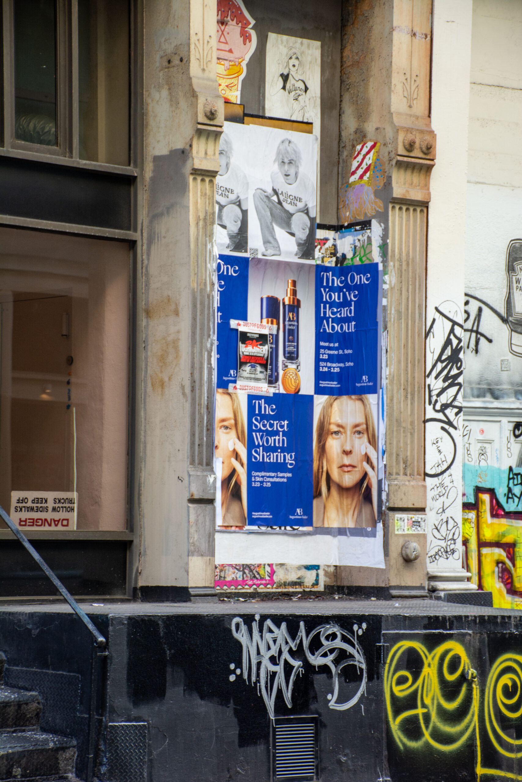 Posters of a woman advertising Augustinus Bader hair care on a wall with graffiti and flyers.