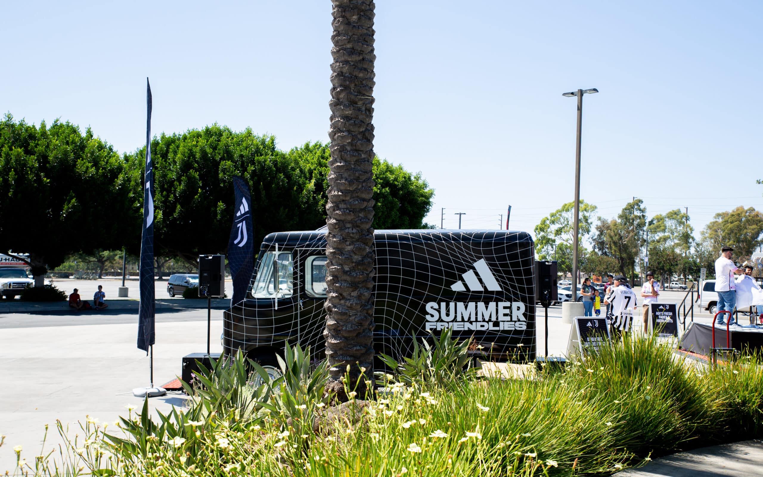 Black Adidas Chevy P10 van labeled SUMMER FRIENDLIES parked by greenery and a palm tree.