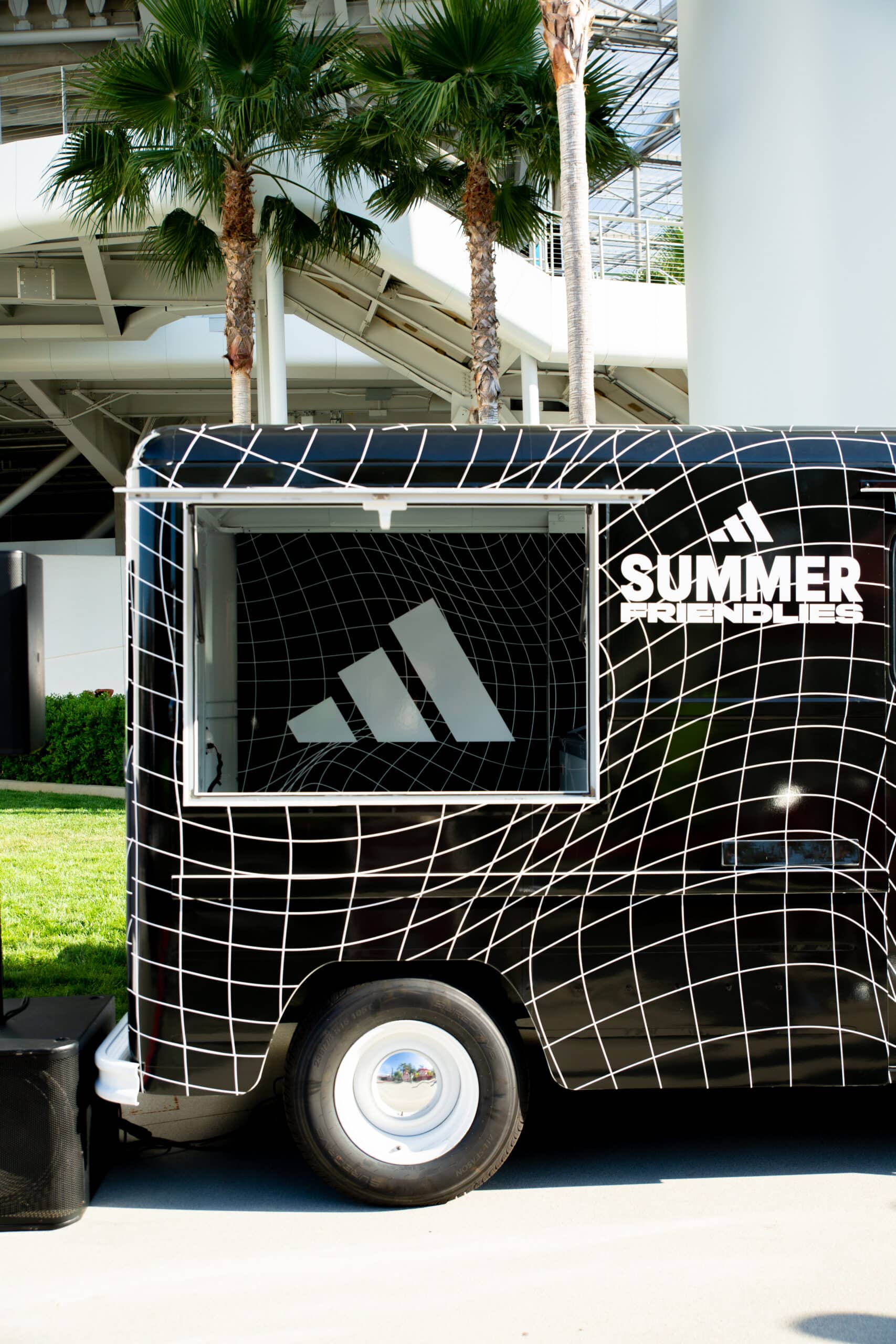 Black Chevy P10 food truck with Adidas logo and SUMMER FRIENDLIES text, parked by palm trees.