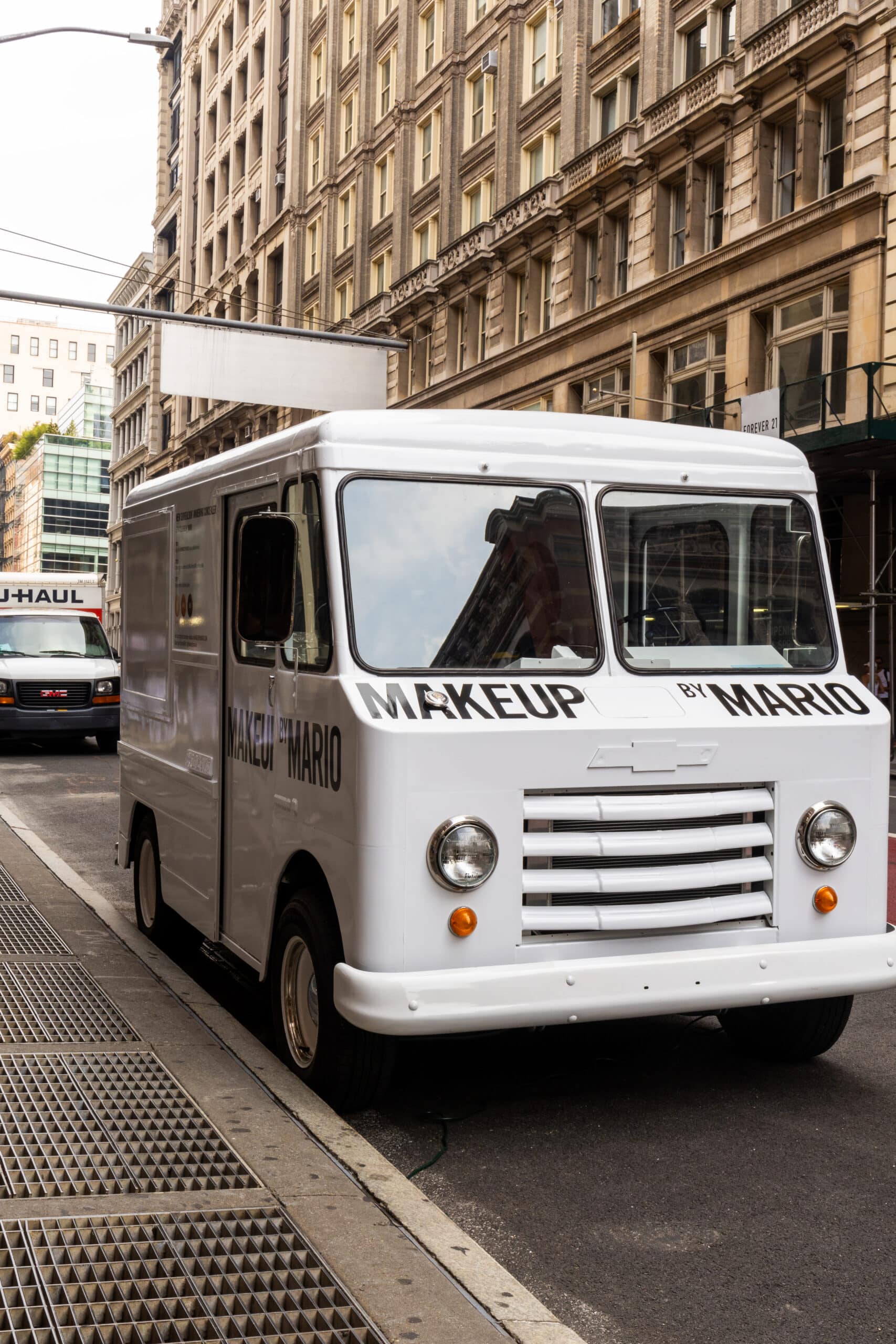 White Chevy P10 delivery truck labeled MAKEUP BY MARIO parked on a city street with tall buildings.