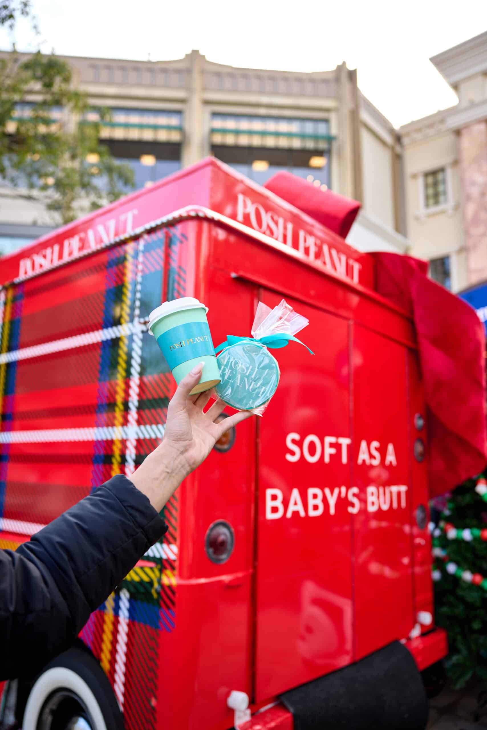 Hand holding teal cup and item in front of red plaid truck with "SOFT AS A BABY'S BUTT" text.