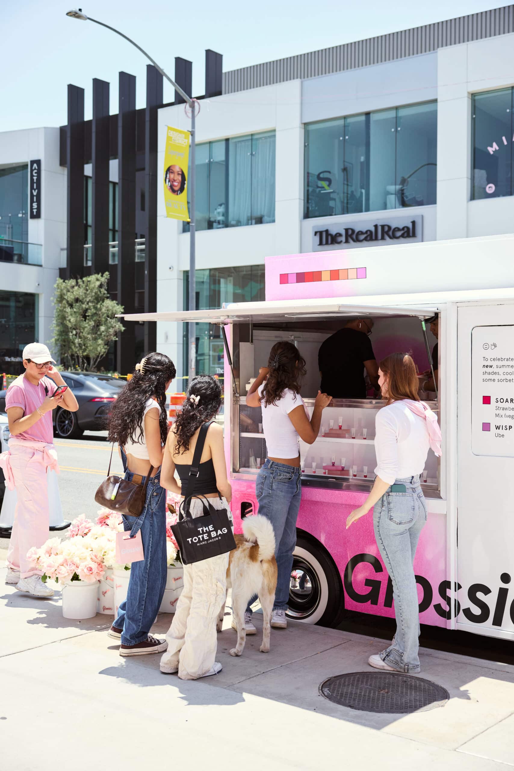 Young women and a dog stand by a pink Metro Mite beauty truck on a city street.