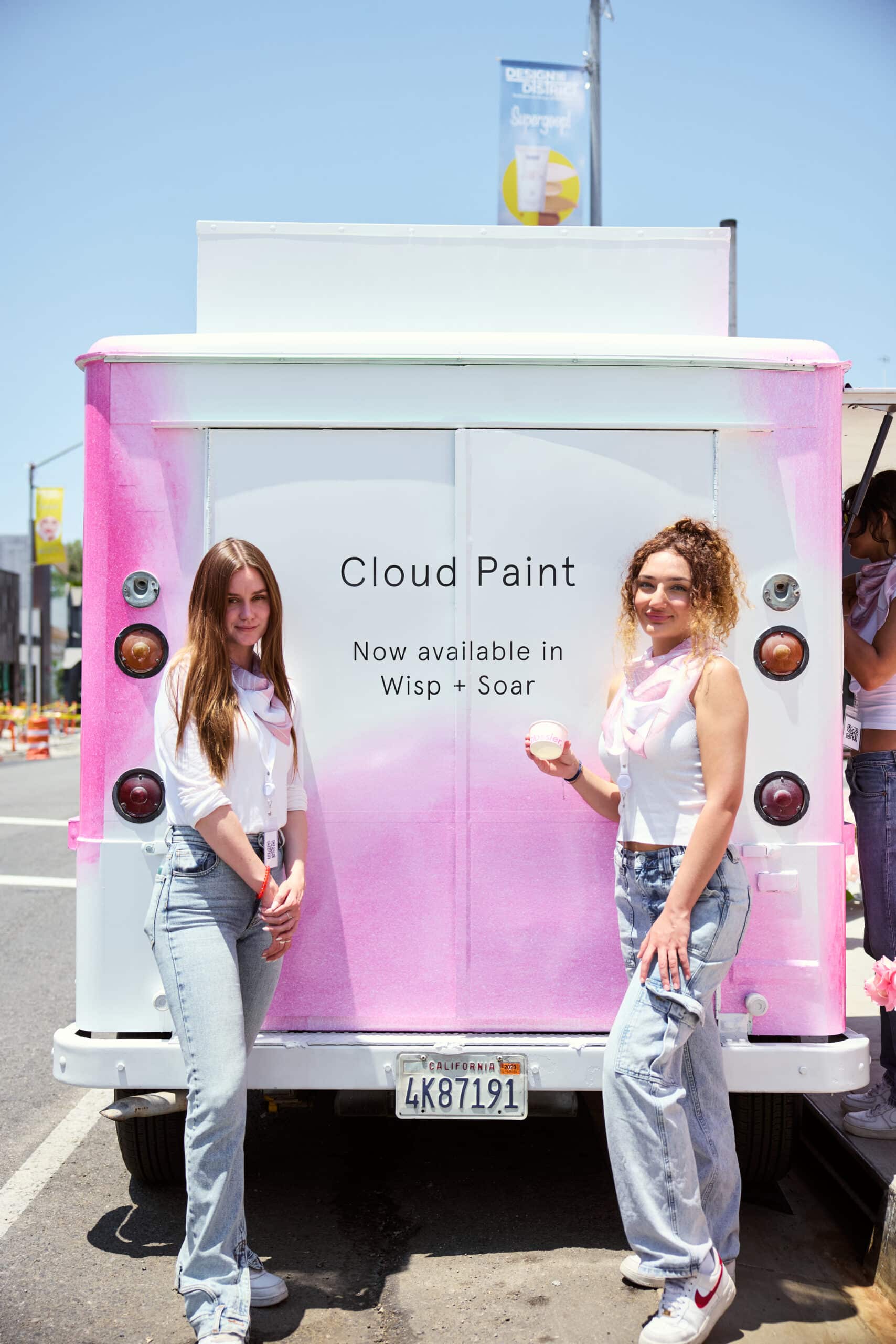 Two women in white tops and jeans smile by a pink Metro Mite truck with a Cloud Paint sign.