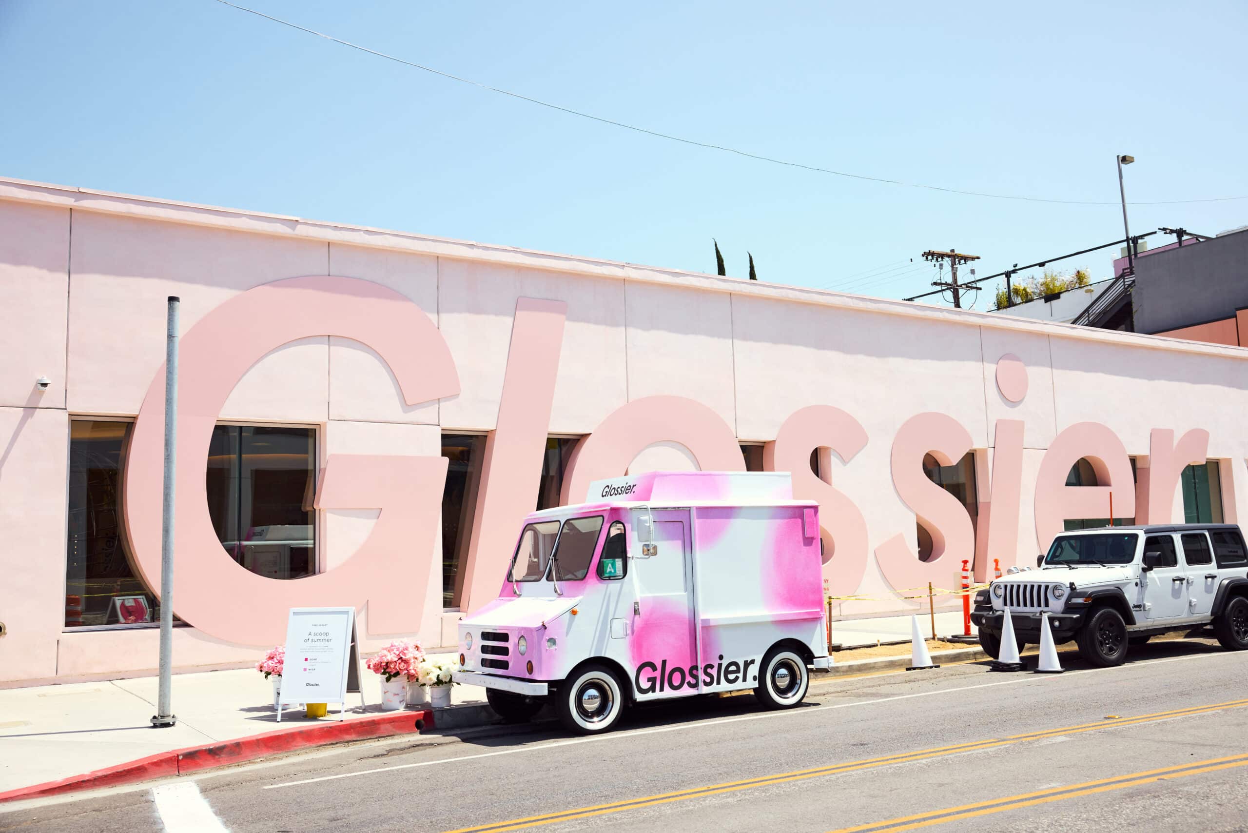 Pink and white Glossier truck parked in front of large pink building labeled Glossier.