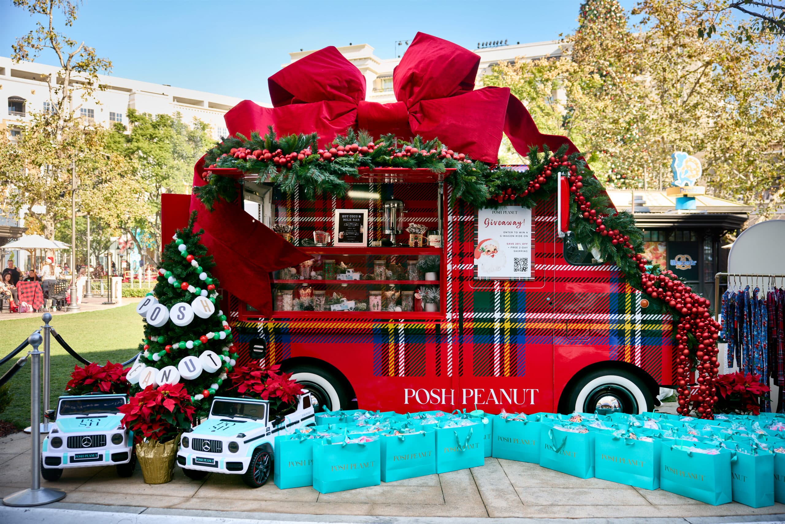 Red truck with holiday decorations, jars, gifts, blue gift bags, toy cars, and poinsettias in front.