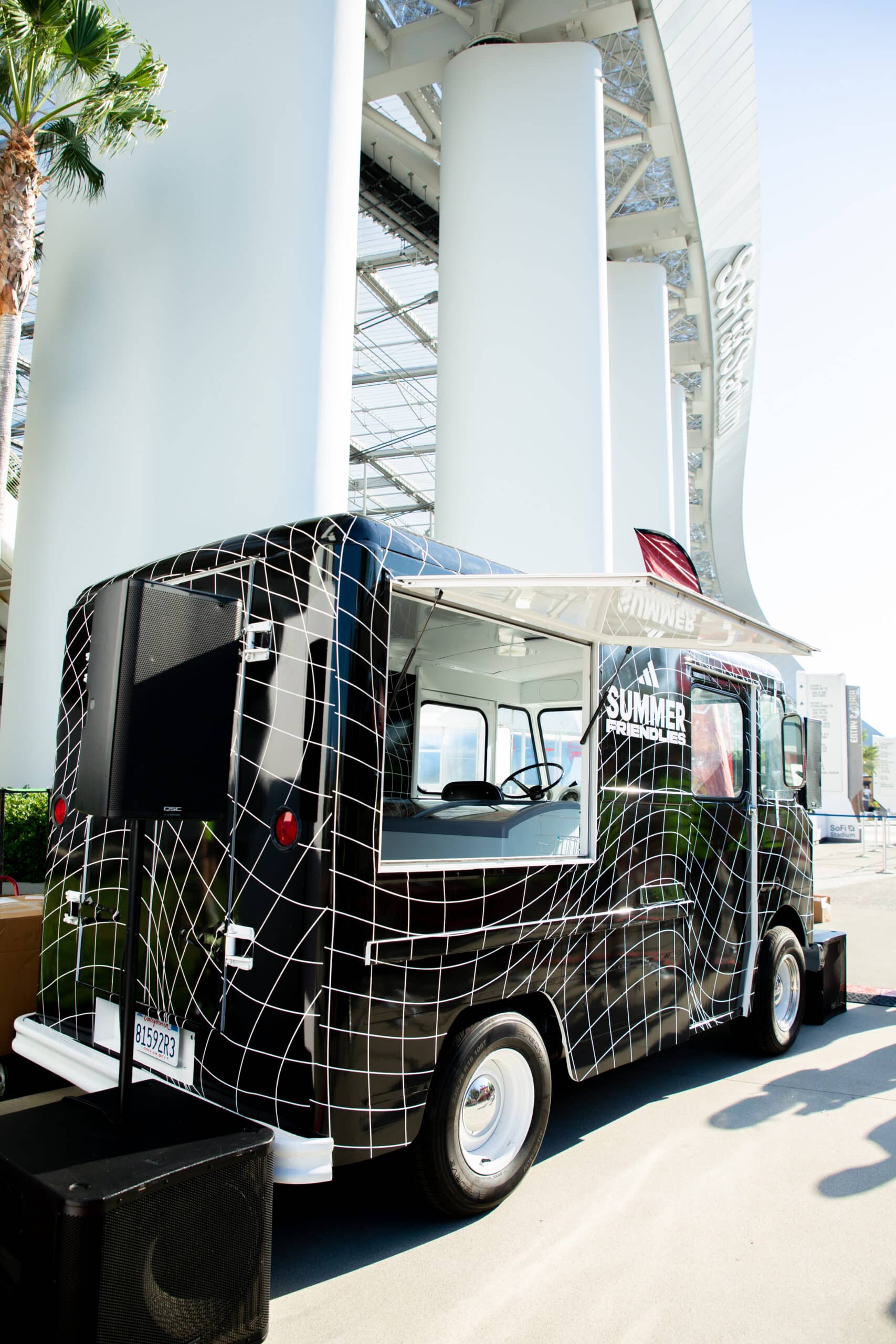 Black Chevy P10 food truck with white grid parked under modern structure on a sunny day.