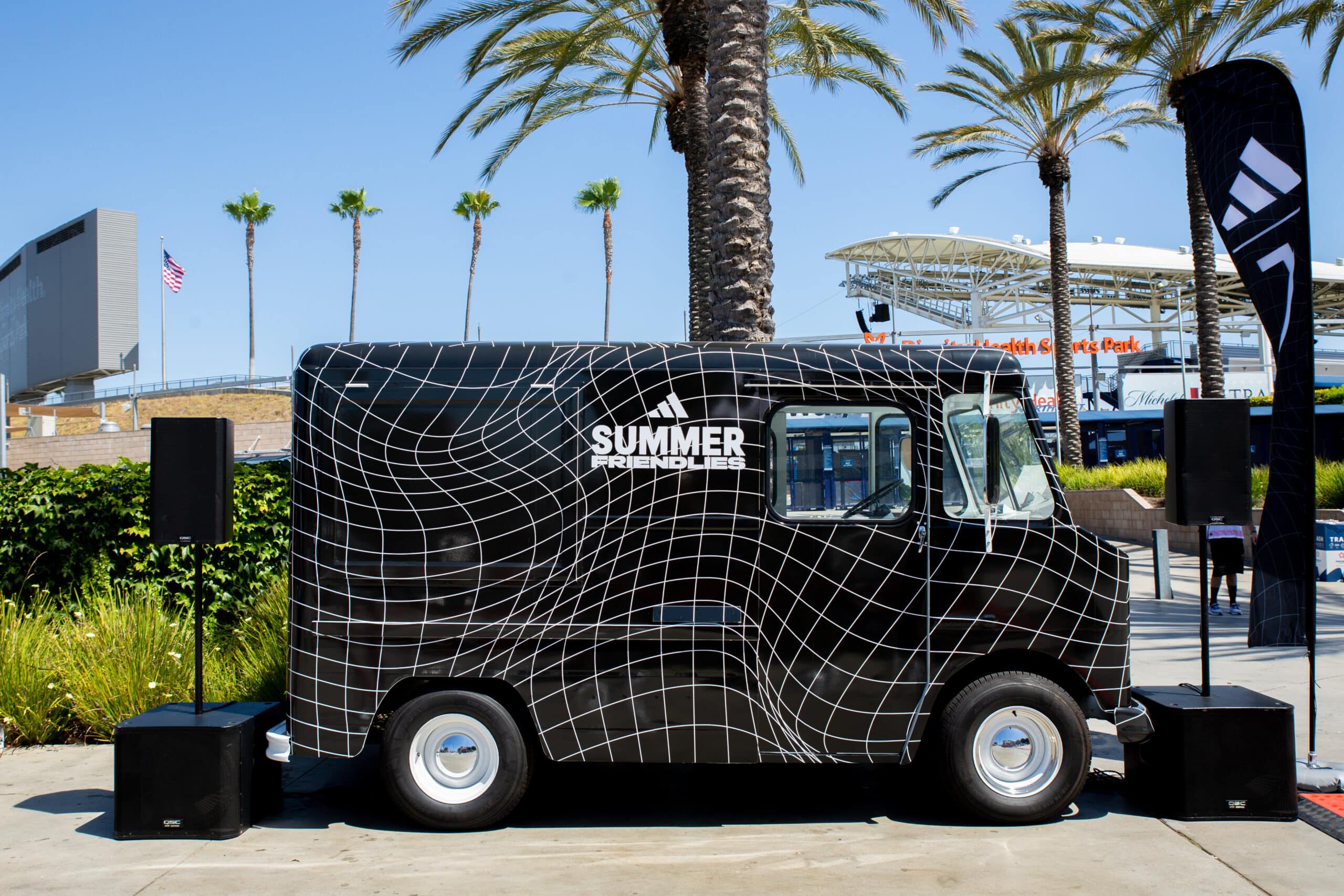 Black Chevy P10 food truck labeled SUMMER FRIENDLIES, parked by palm trees and a stadium.