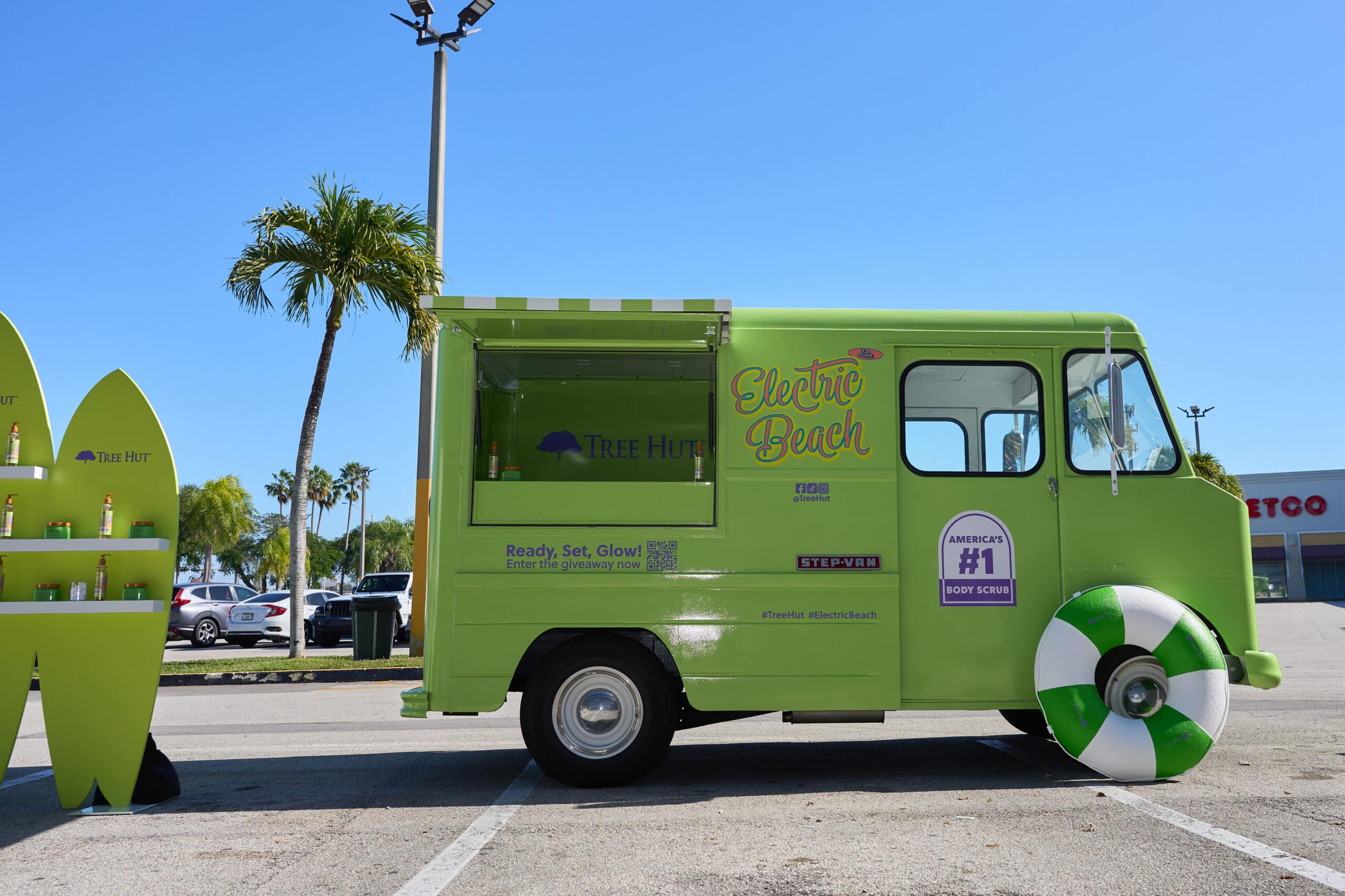 Green Chevy P10 food truck labeled Electric Beach by palm trees, with shelf and beach ball in front.