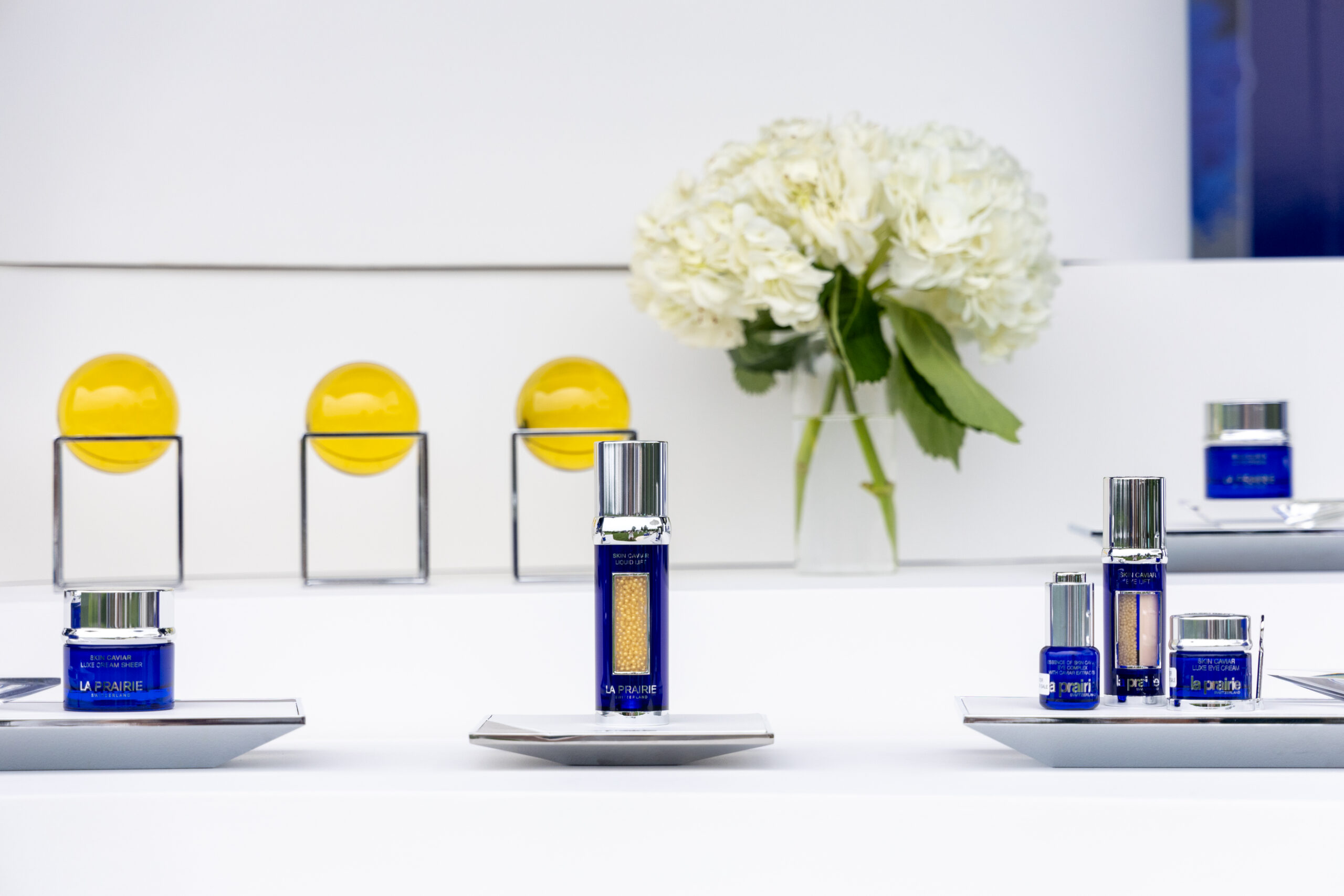 Blue skincare containers on silver trays with white flowers and yellow ornaments in the background.