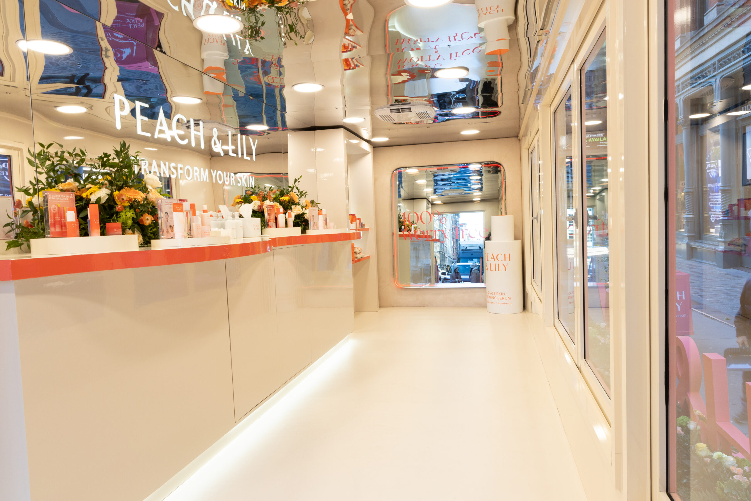 Peach & Lily pop-up store with shelves of skincare, floral accents, and a pop-up bus outside.