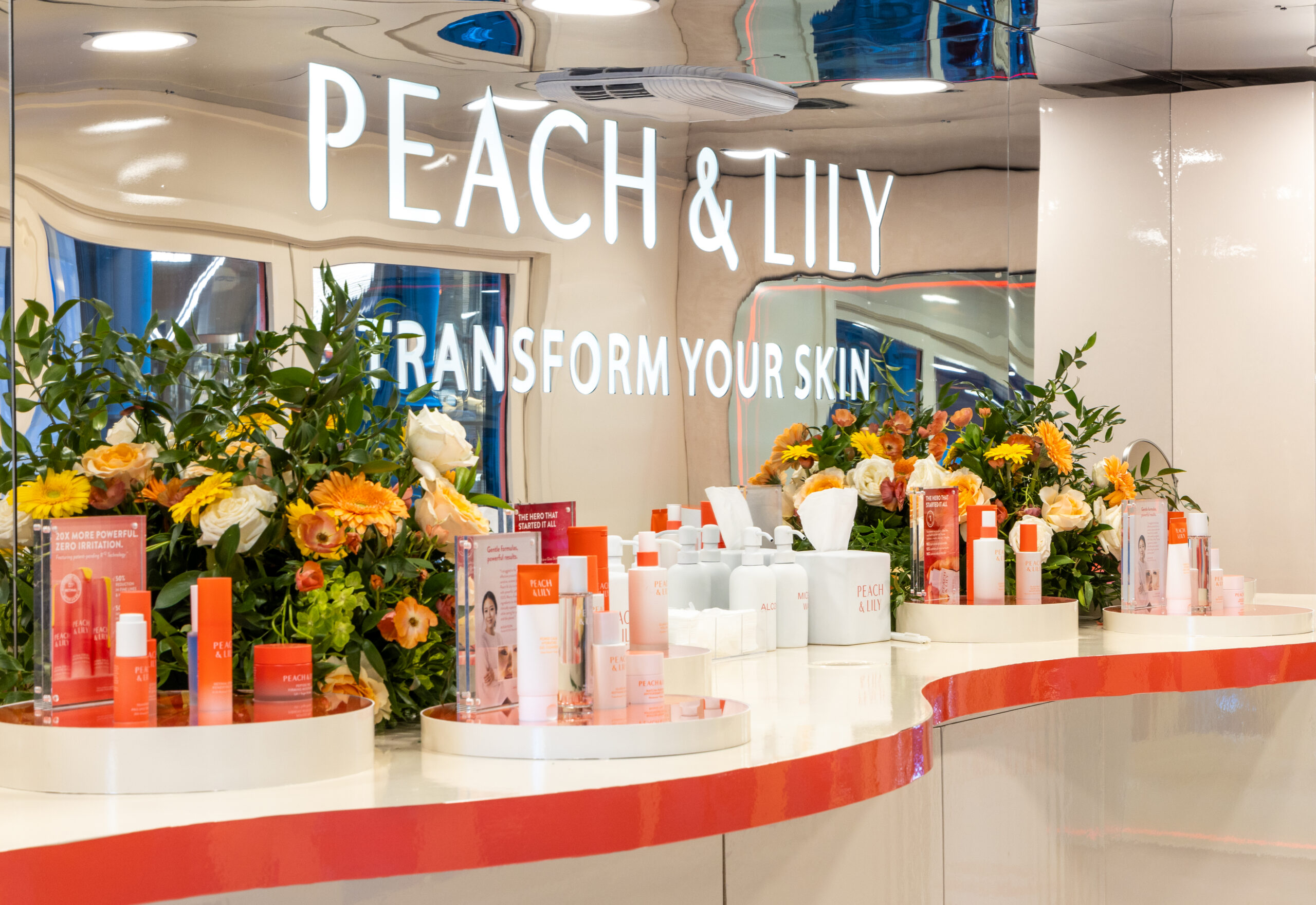 Peach & Lily skincare display with bottles, boxes, flowers, and sign inside branded pop-up bus.