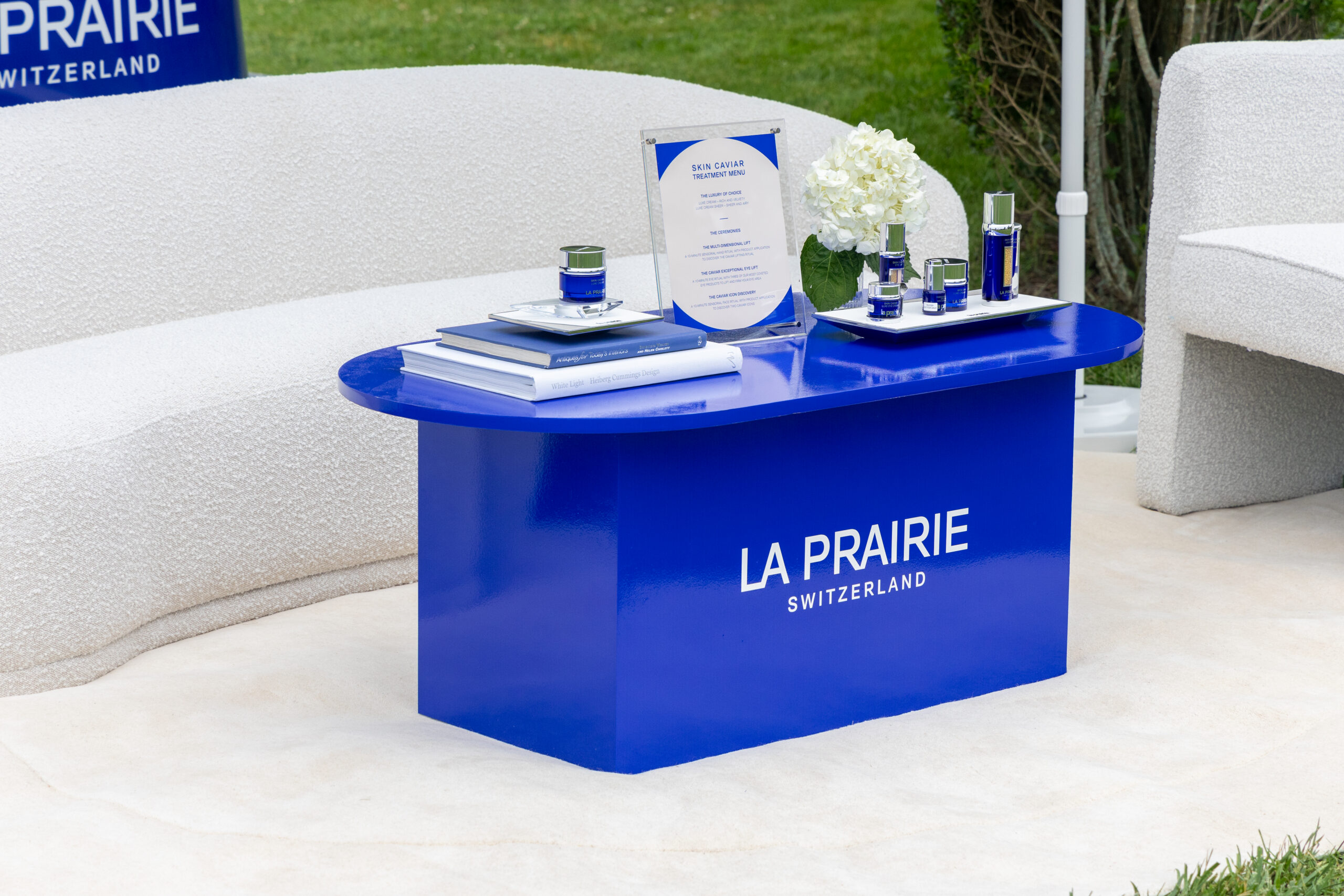 La Prairie pop-up table with skincare, flowers, and brochures, surrounded by white chairs outdoors.