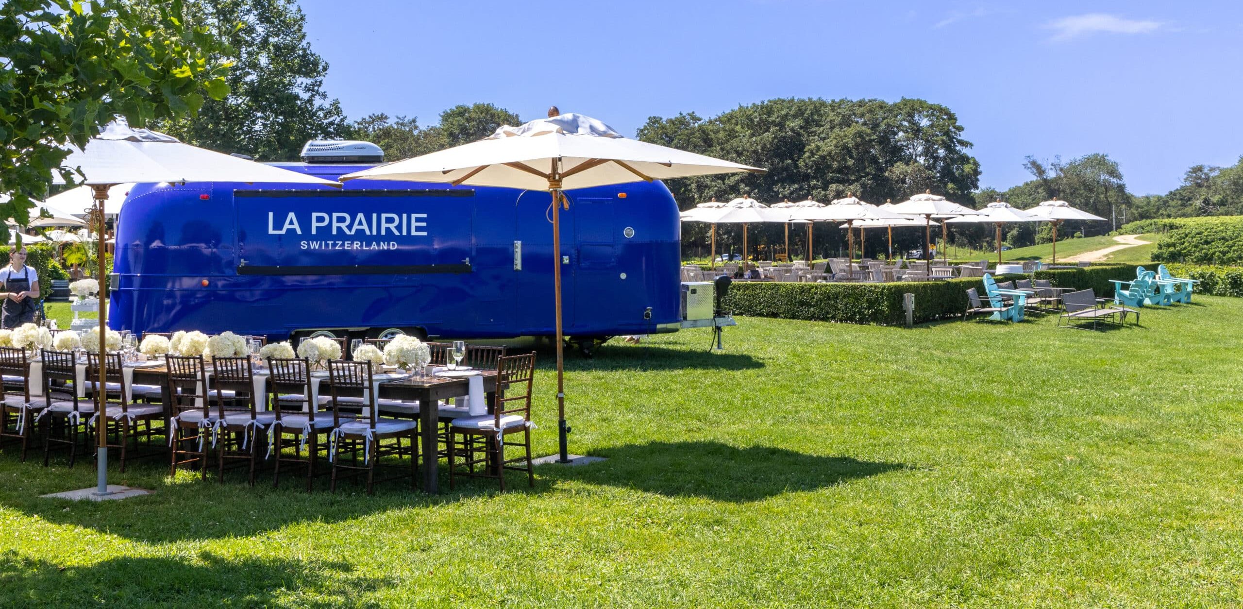 Blue La Prairie trailer on grass beside a long table with white flowers and umbrellas.
