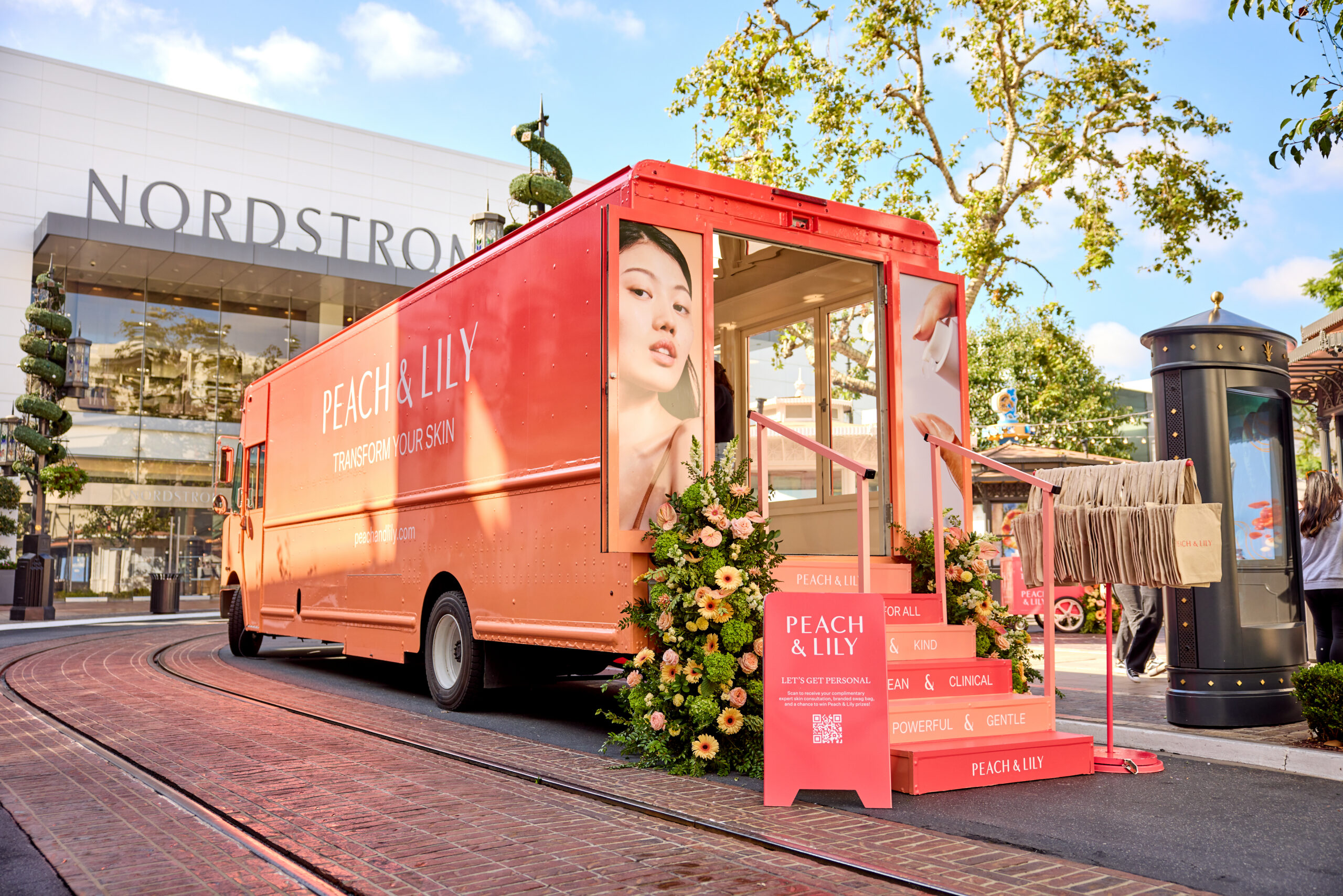 Peach & Lily peach pop-up bus with flower decor and large face images parked outside Nordstrom.
