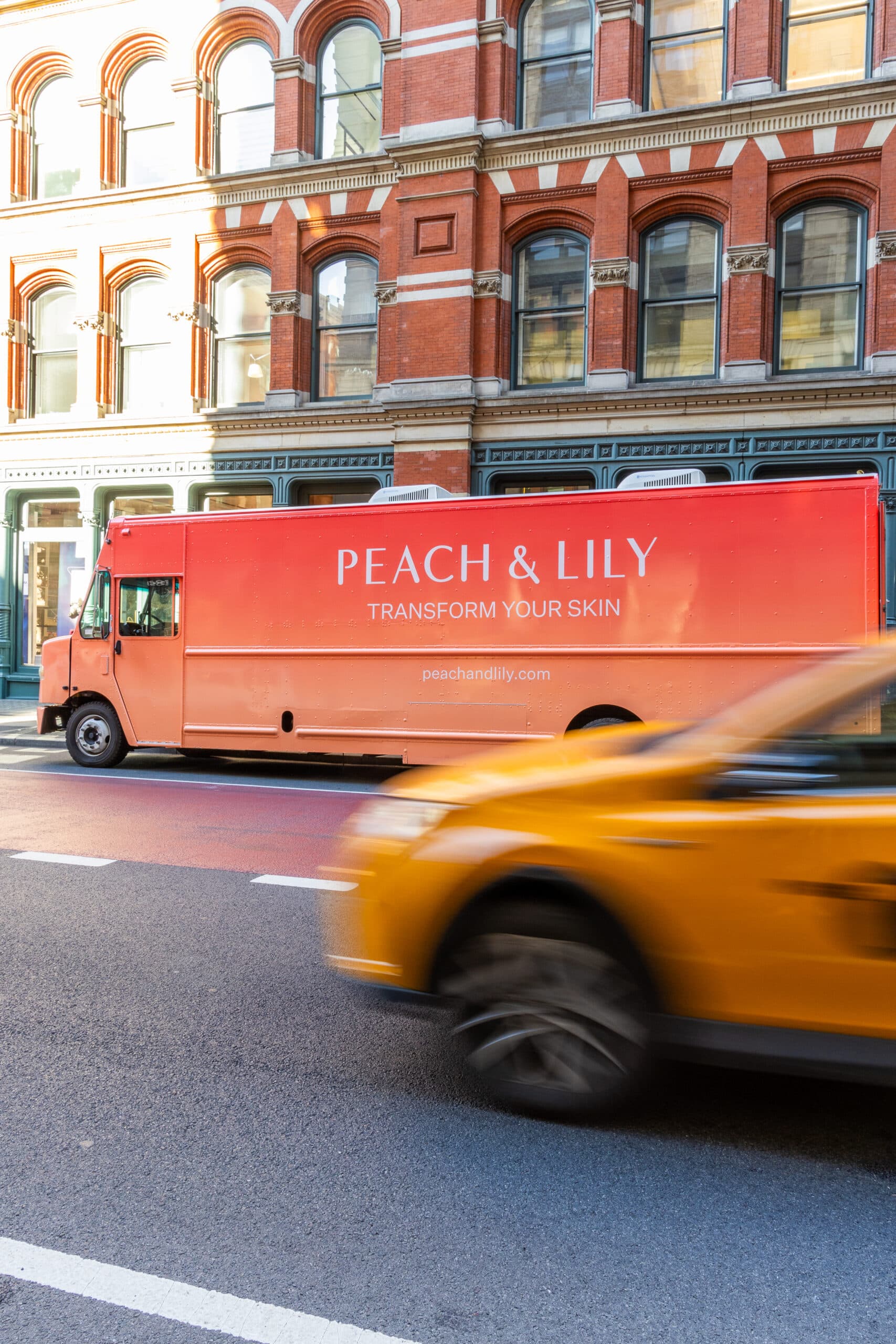 Peach & Lily pop-up bus with “Transform Your Skin” parked on city street; yellow car passes.