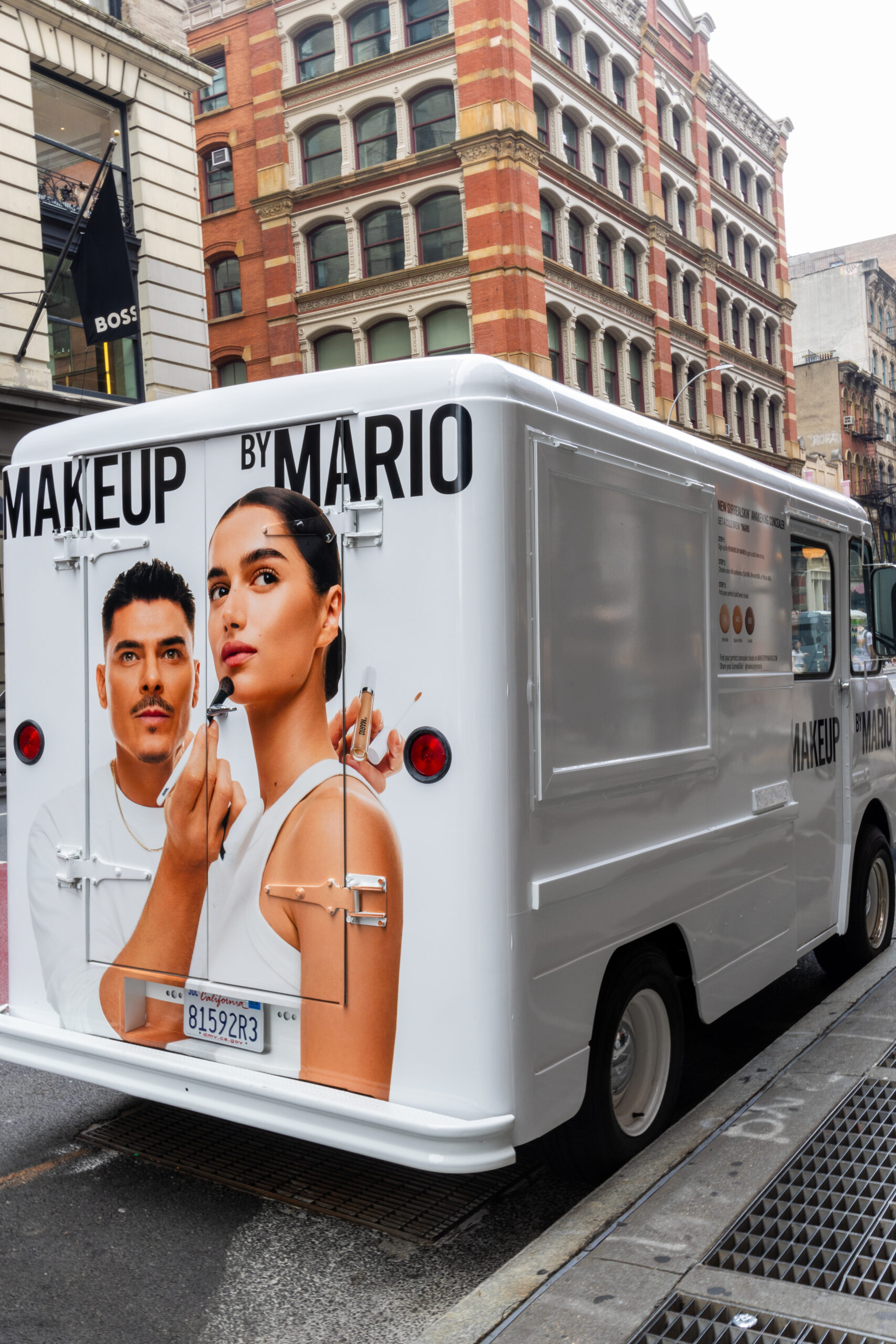 A white van with a Makeup by Mario ad showing a man and woman applying makeup on a city street.