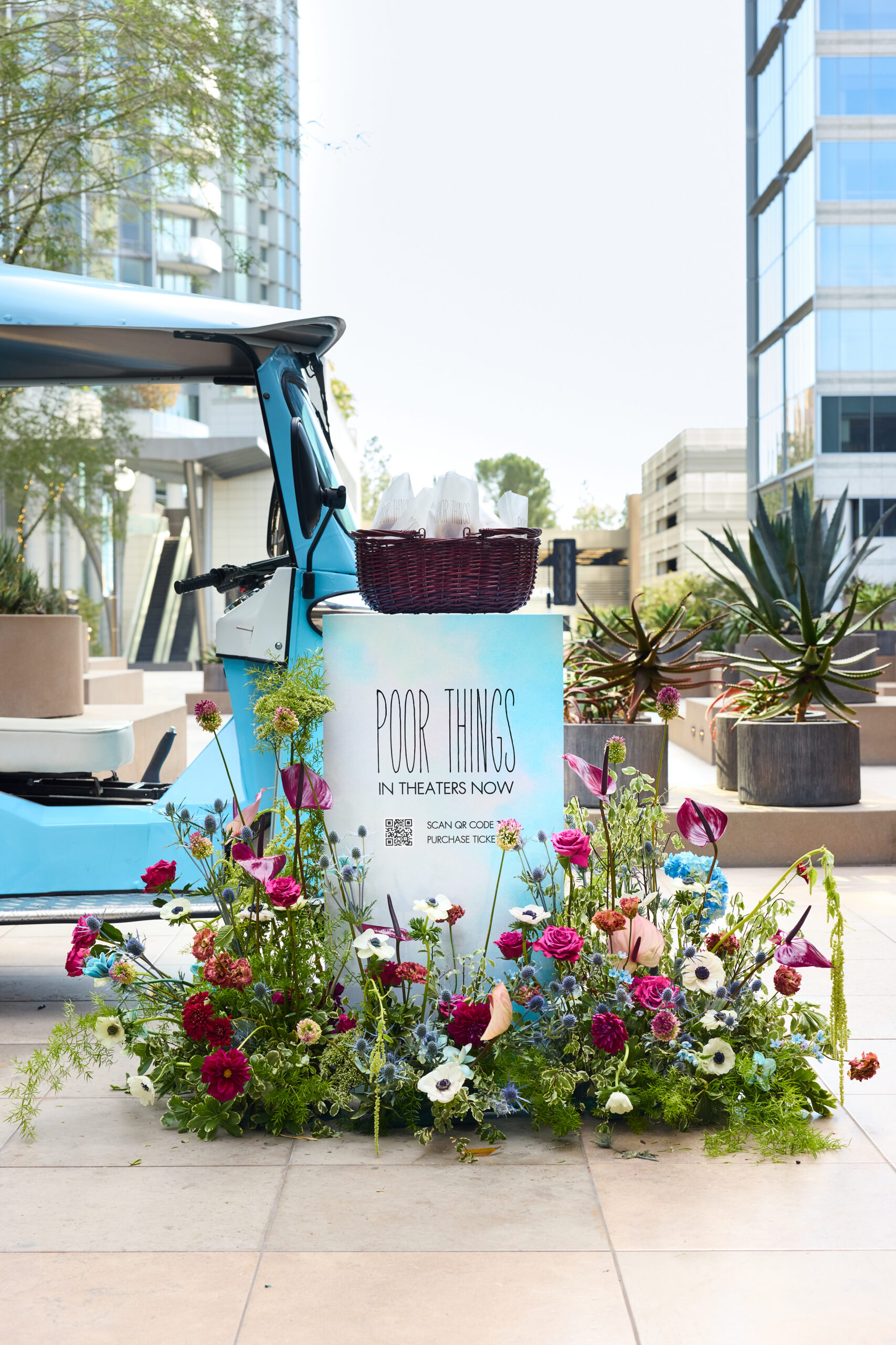 Blue Peach & Lily pop-up bus beside a "Poor Things In Theaters Now" display with flowers and basket.