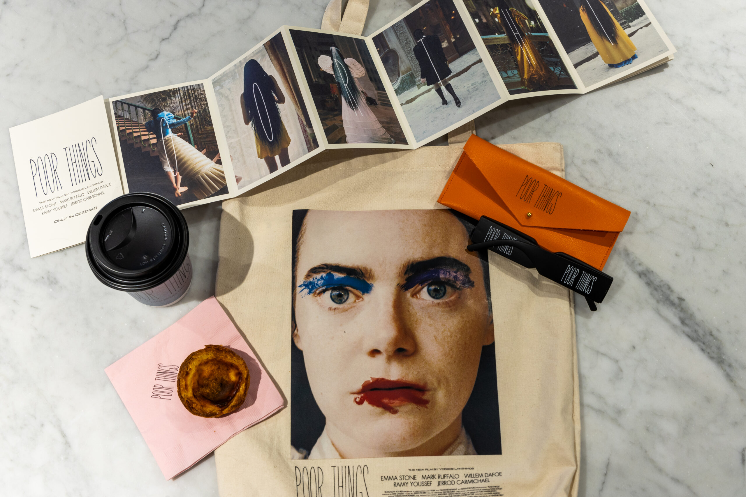 Tote bag, movie poster, coffee cup, pastry, bus ticket, glasses case, ribbon, and photos on marble.