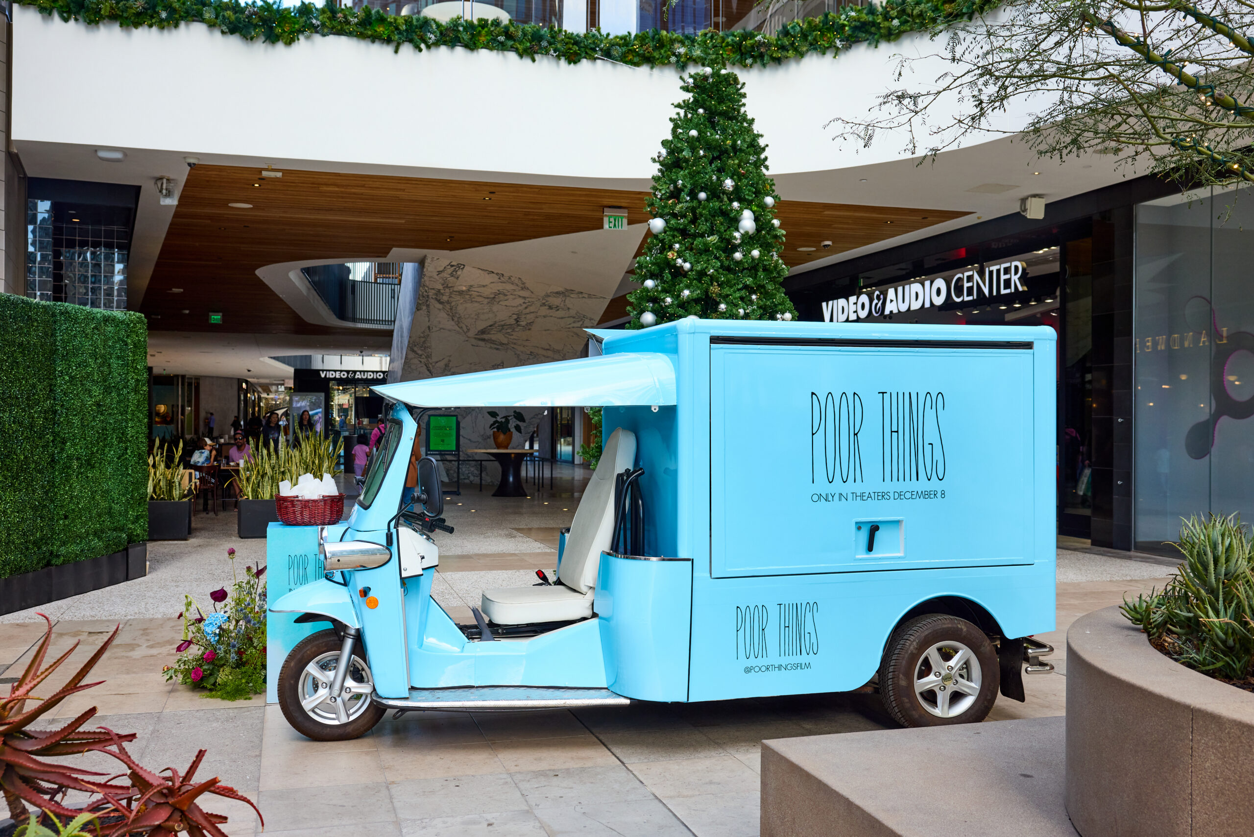 A light blue Peach & Lily pop-up bus with "Poor Things" is parked by a decorated Christmas tree.