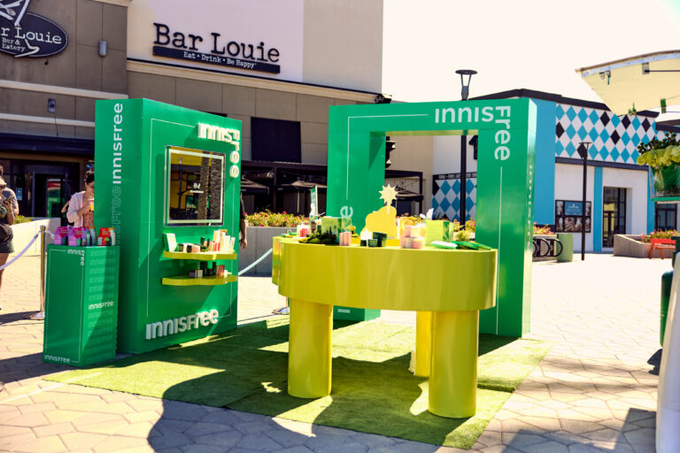 Innisfree skincare display with products on tables and shelves on grass at a shopping center.