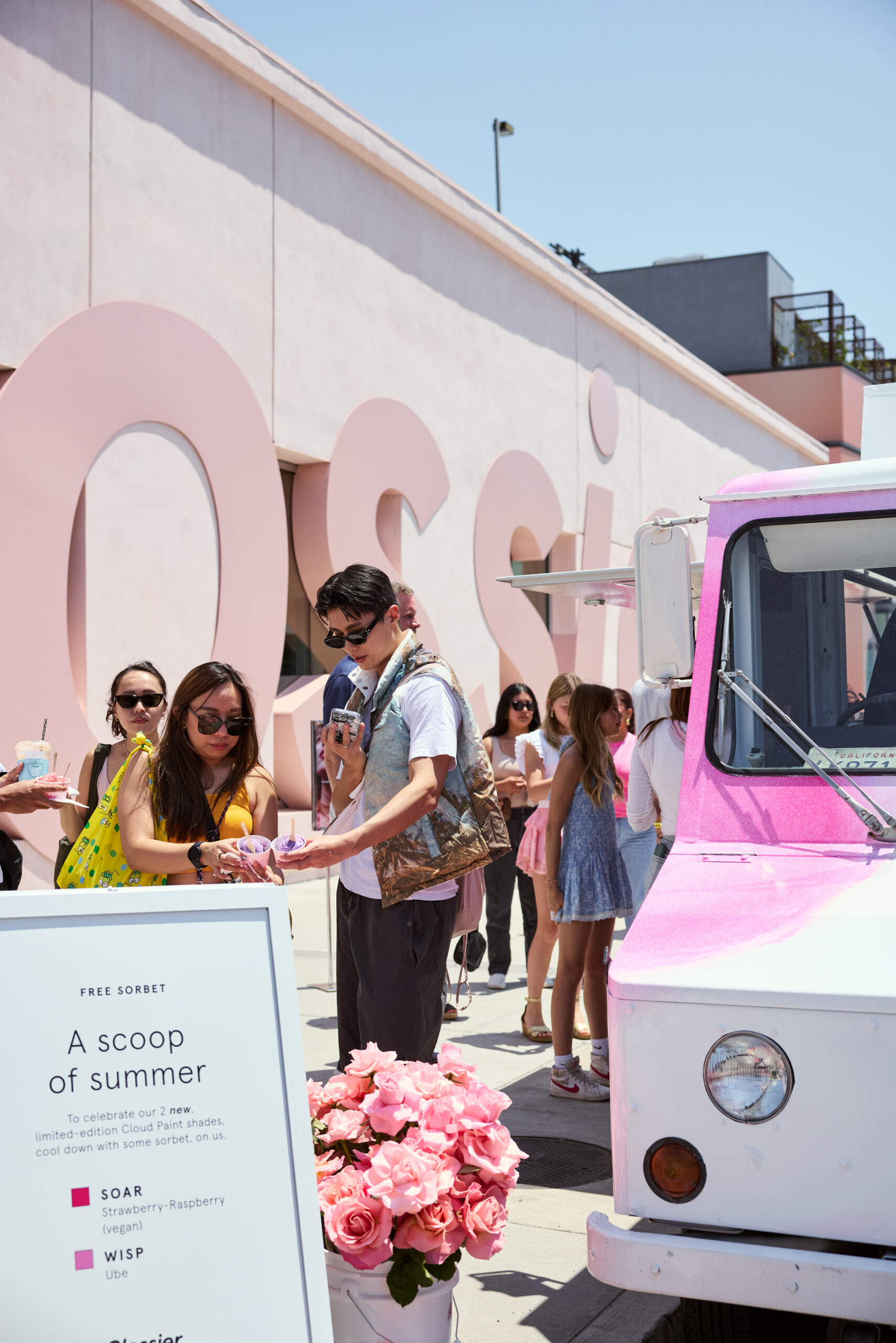 People line up at a pink and white ice cream truck; a sign offers free sorbet nearby.