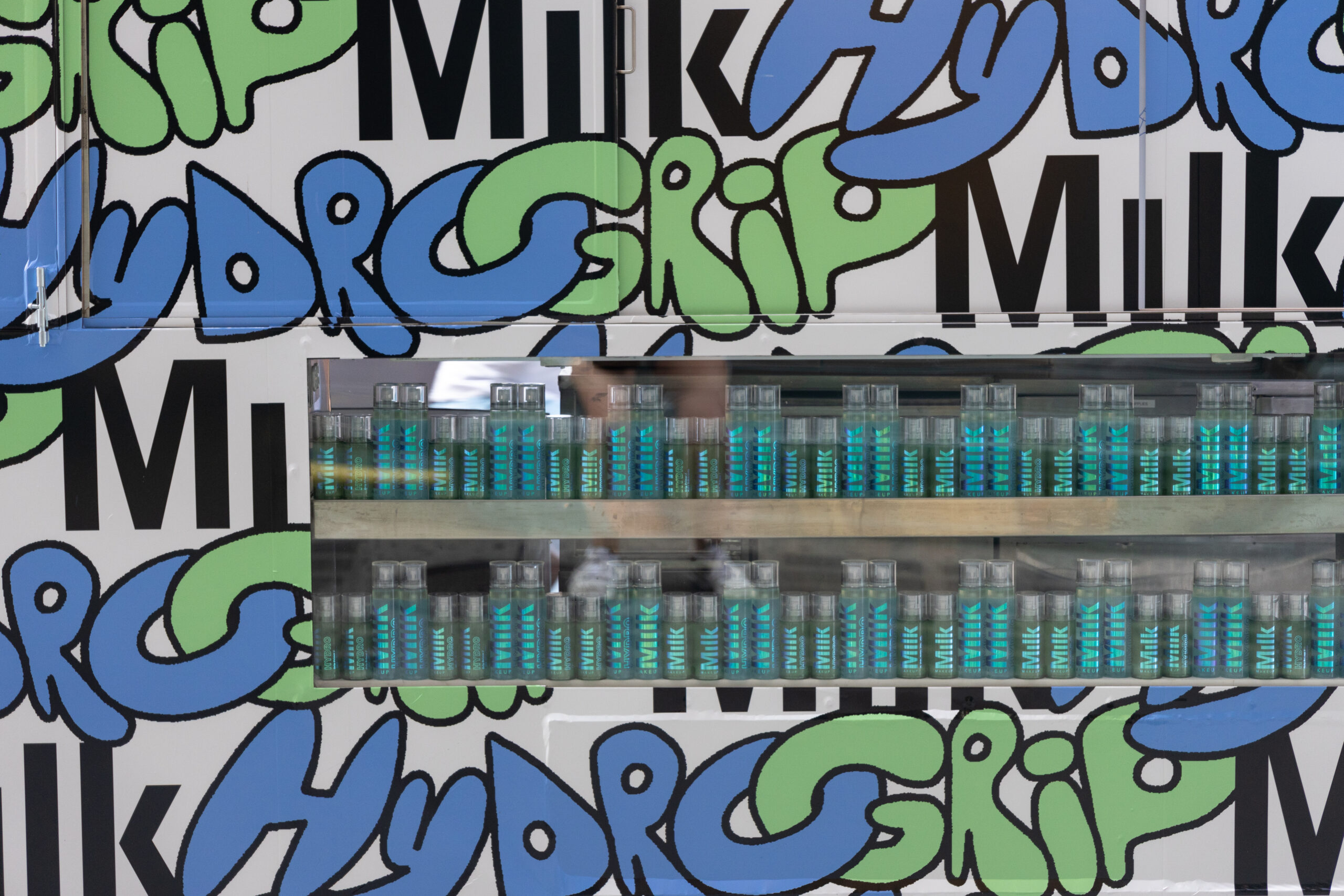 Shelf with blue and green bottles against a wall with repeated words: Milk, Hydro, Grip.