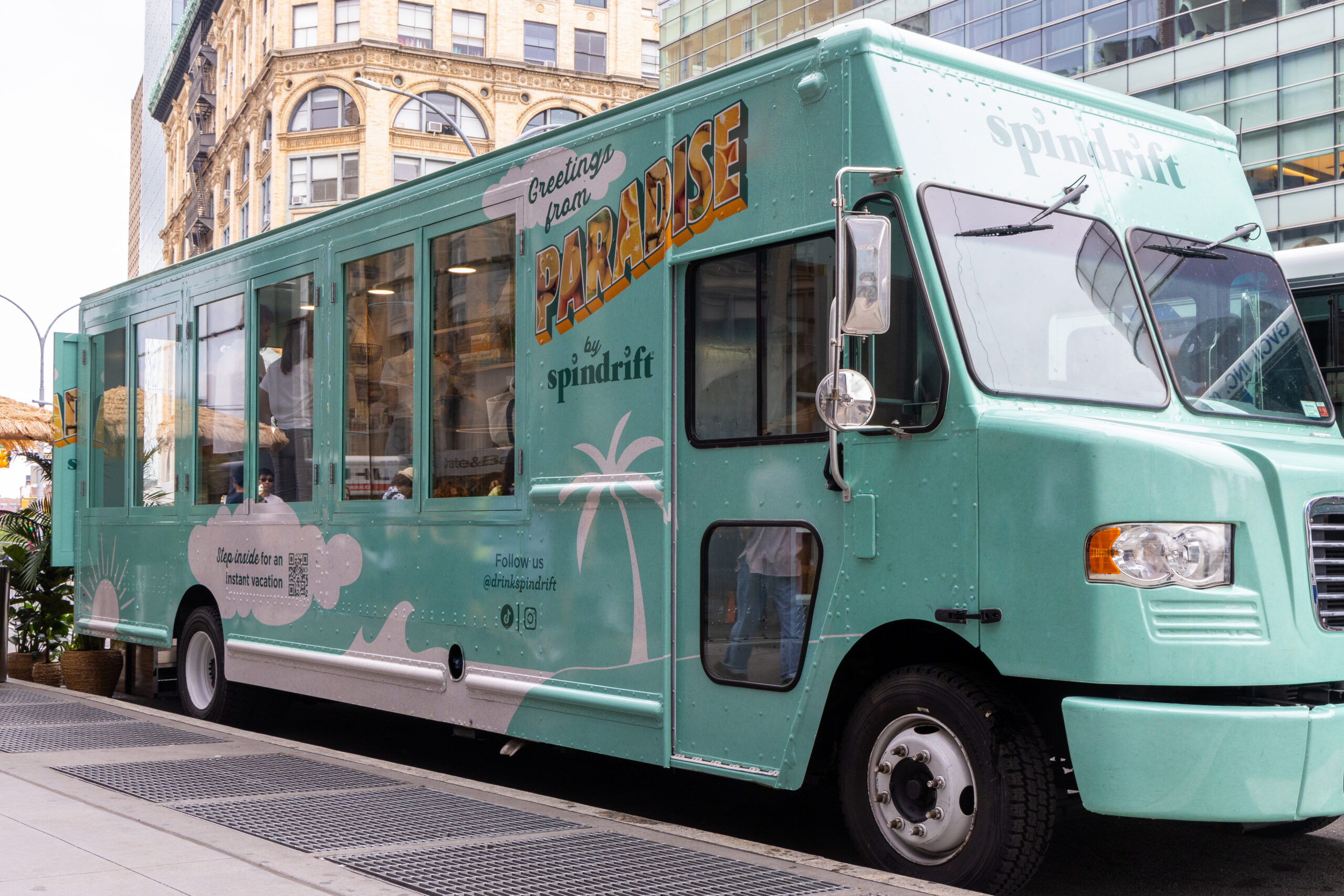 Teal spindrift food truck with palm tree graphics serves drinks on a city street.