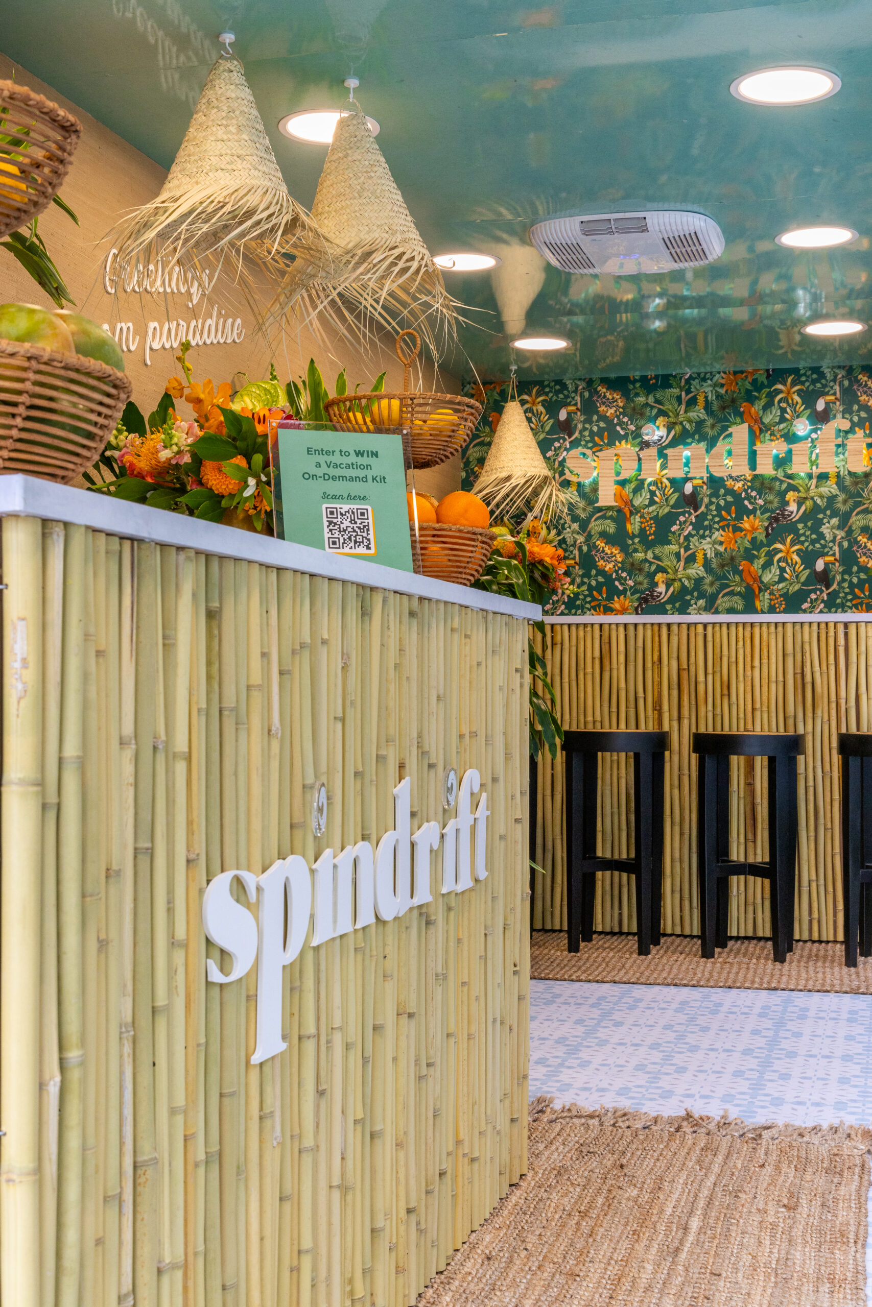 Spindrift pop-up booth with bamboo counter, logo, fruit baskets, barstools, and QR code sign.