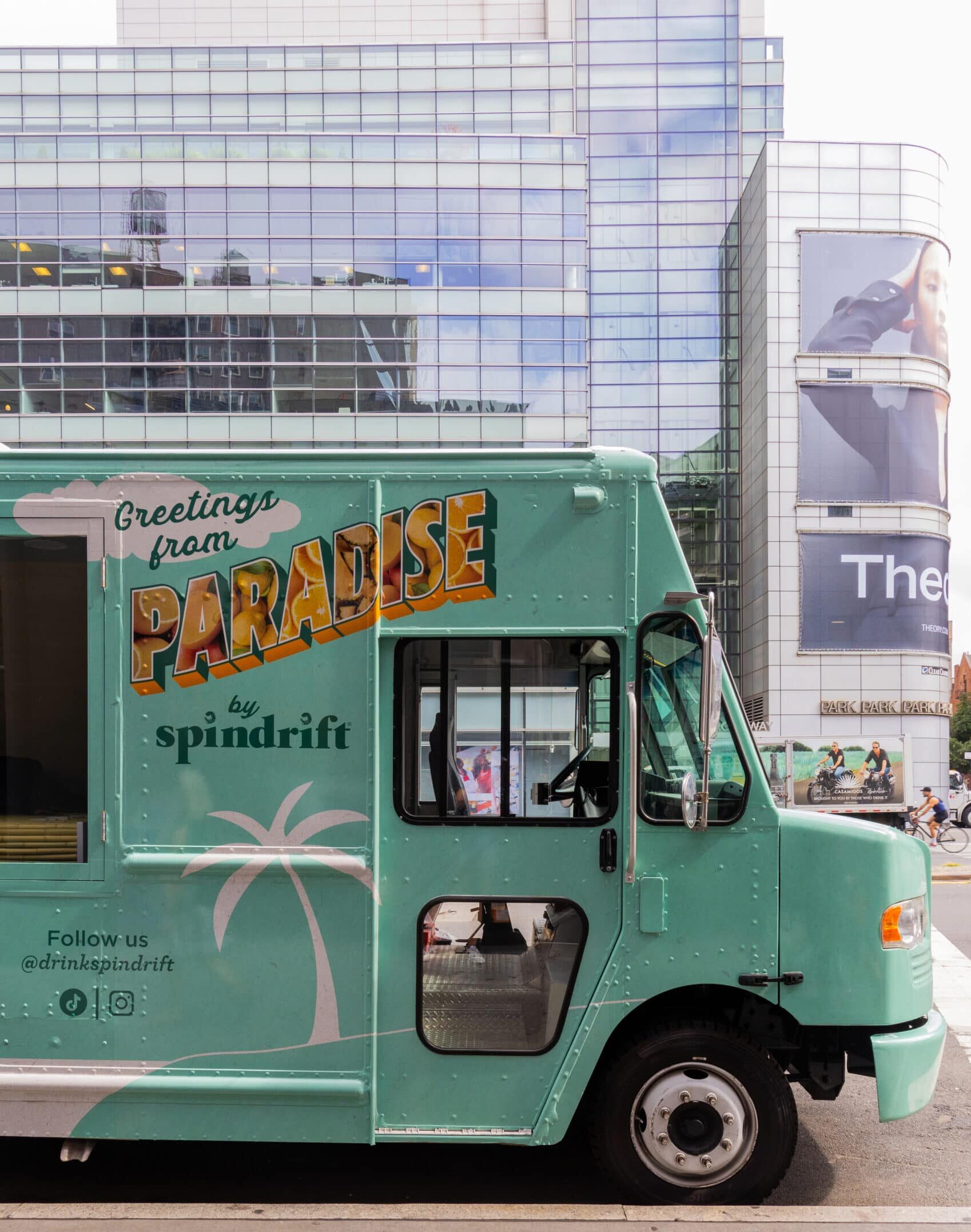 Mint-green Spindrift pop-up food truck parked on a city street with glass buildings nearby.