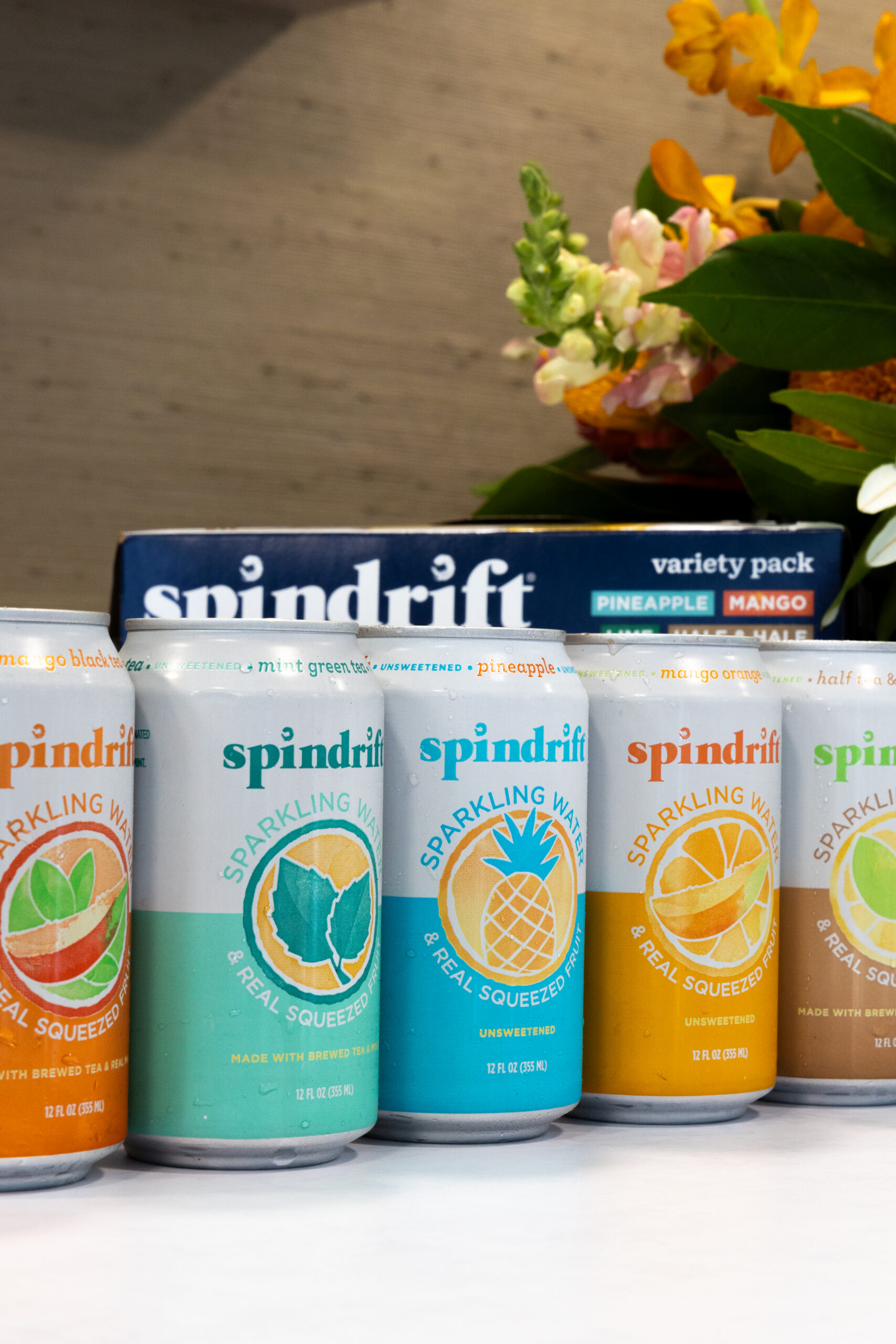Five Spindrift sparkling water cans in various flavors are lined up before a variety pack box.