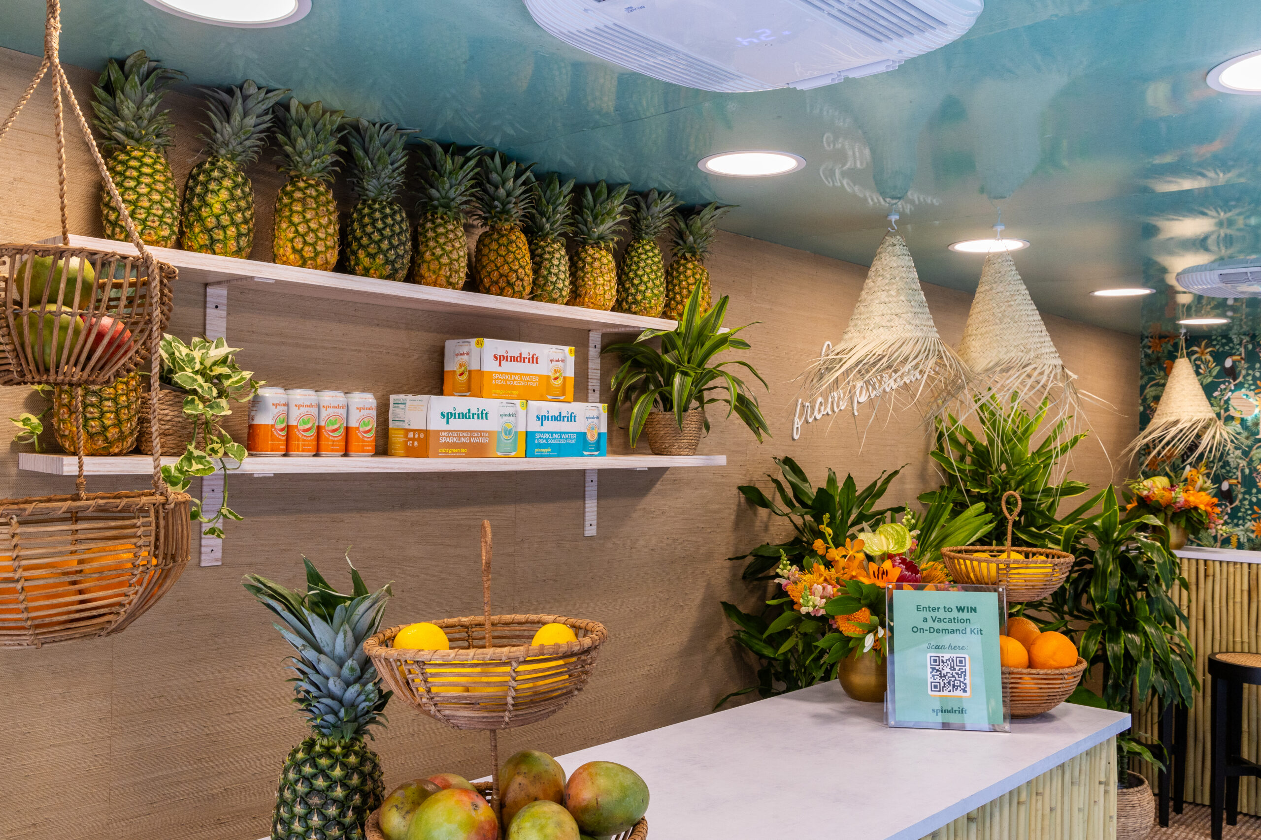Pop-up fruit stand with pineapples, tropical fruits, green plants, juice boxes, and QR code sign.