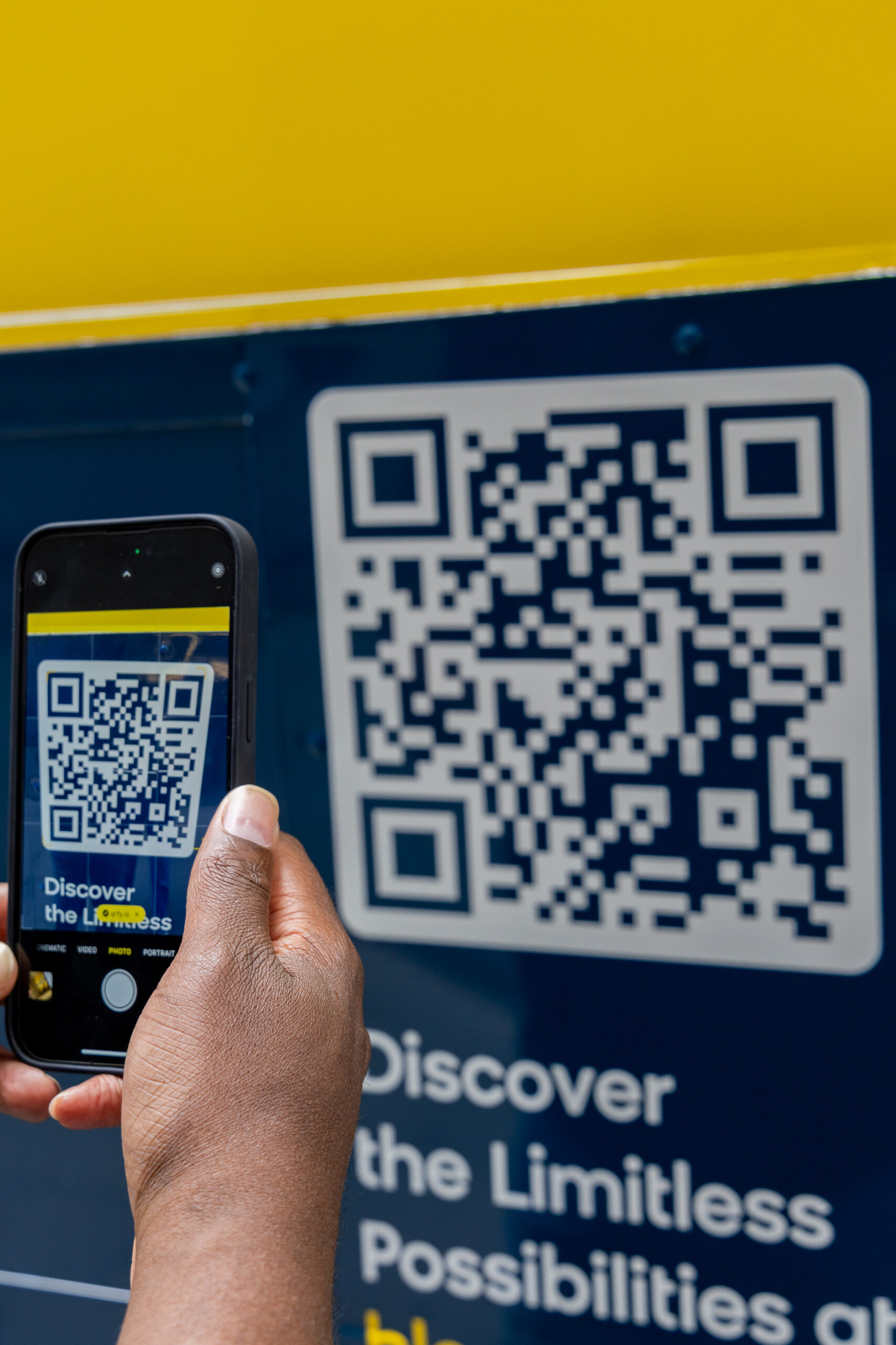 Person scans large QR code with smartphone at popsicle pop-up; blue and yellow background.