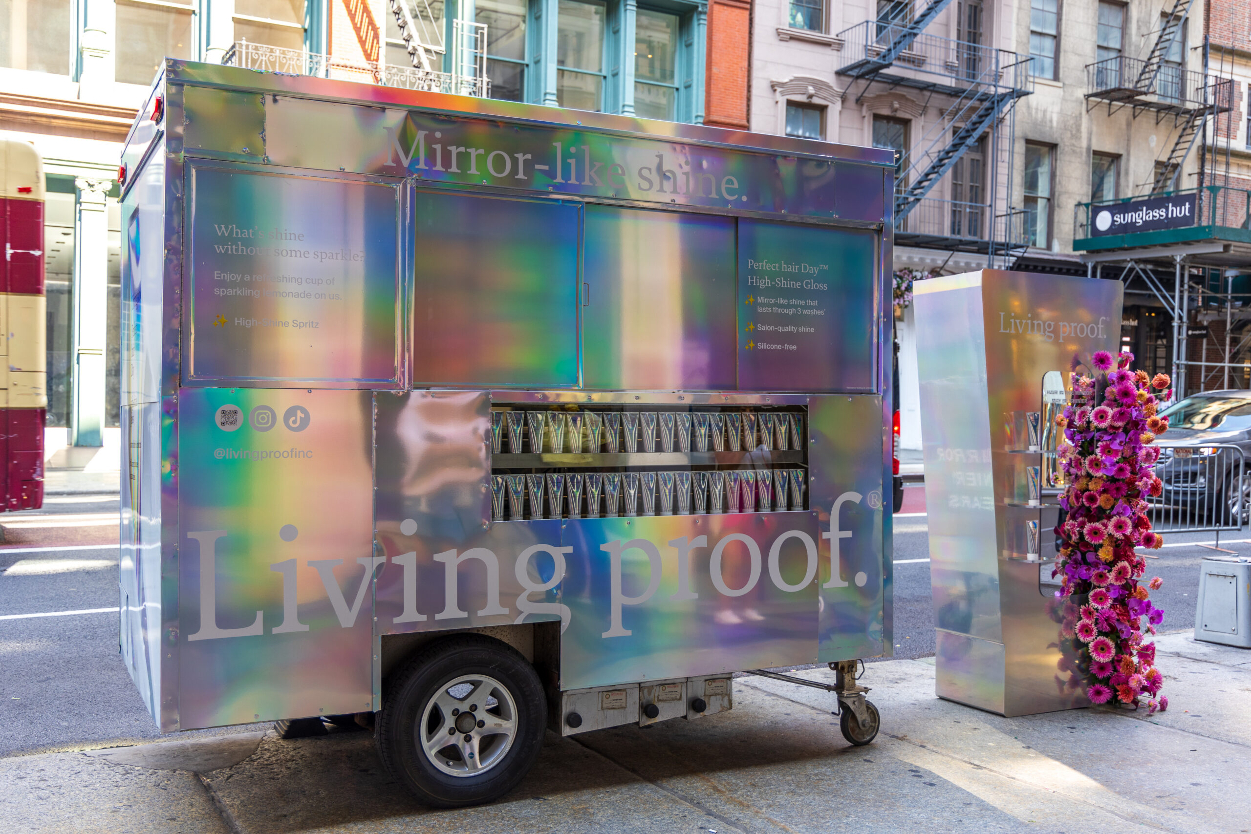 Popsicle cart labeled Living proof with hair products and flowers on a city street.