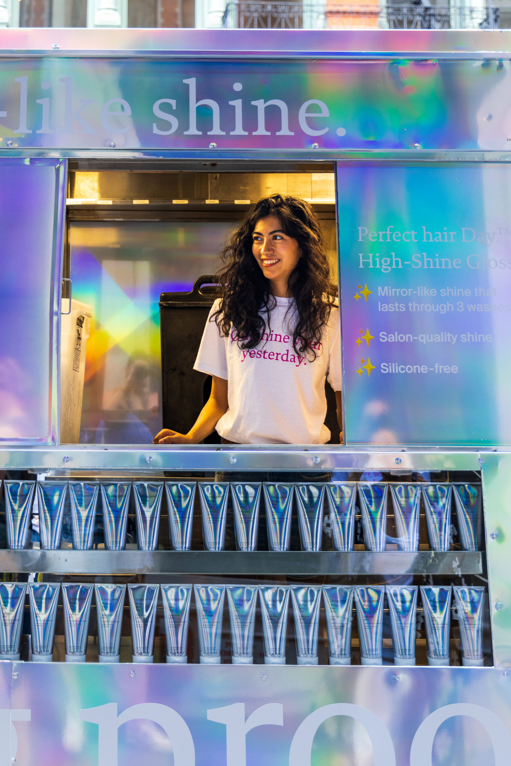 Smiling woman with long curly hair stands in a colorful popsicle booth, lit by bright lights.